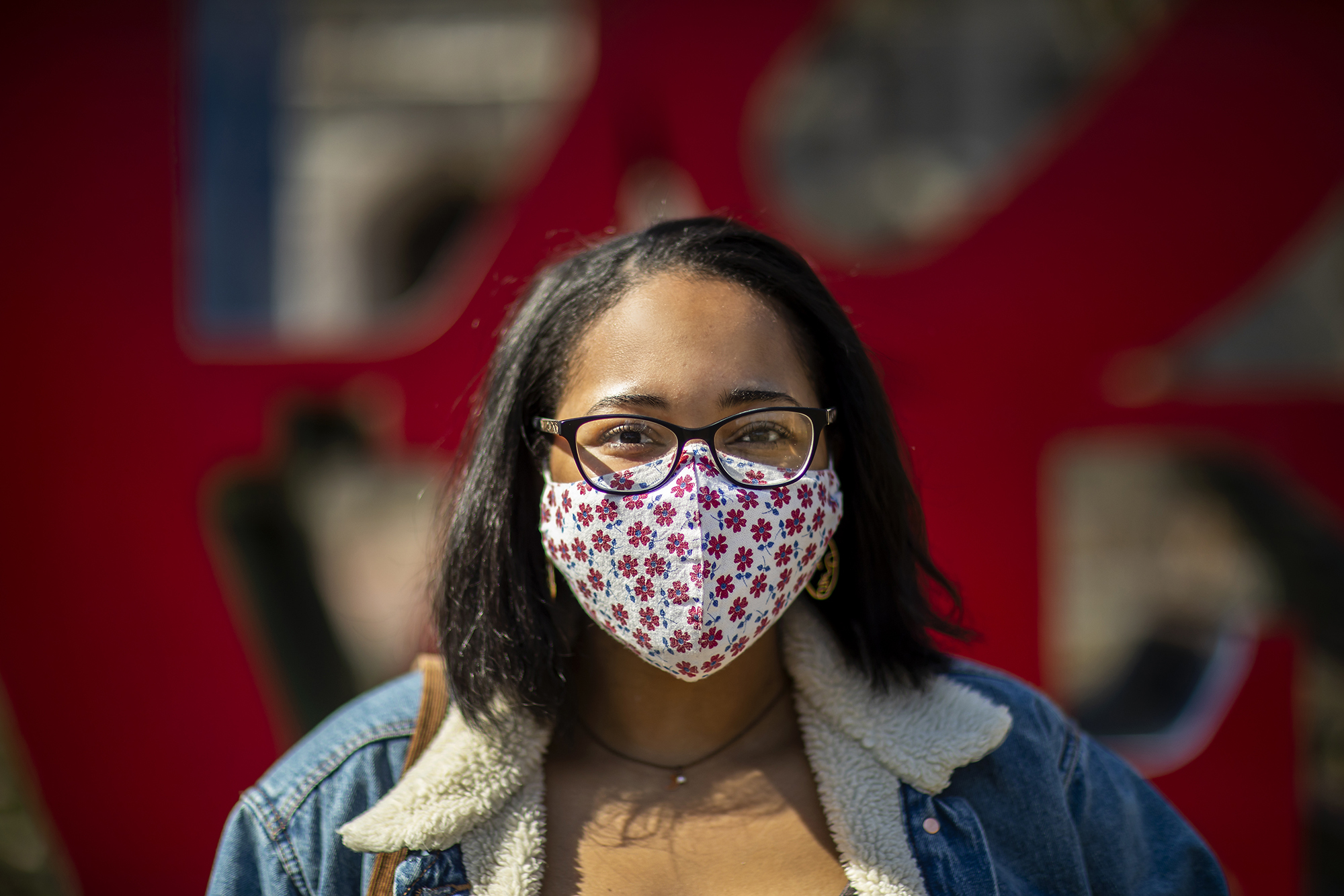 Person smiling behind a floral mask in front of the LOVE statue on Penn’s campus.