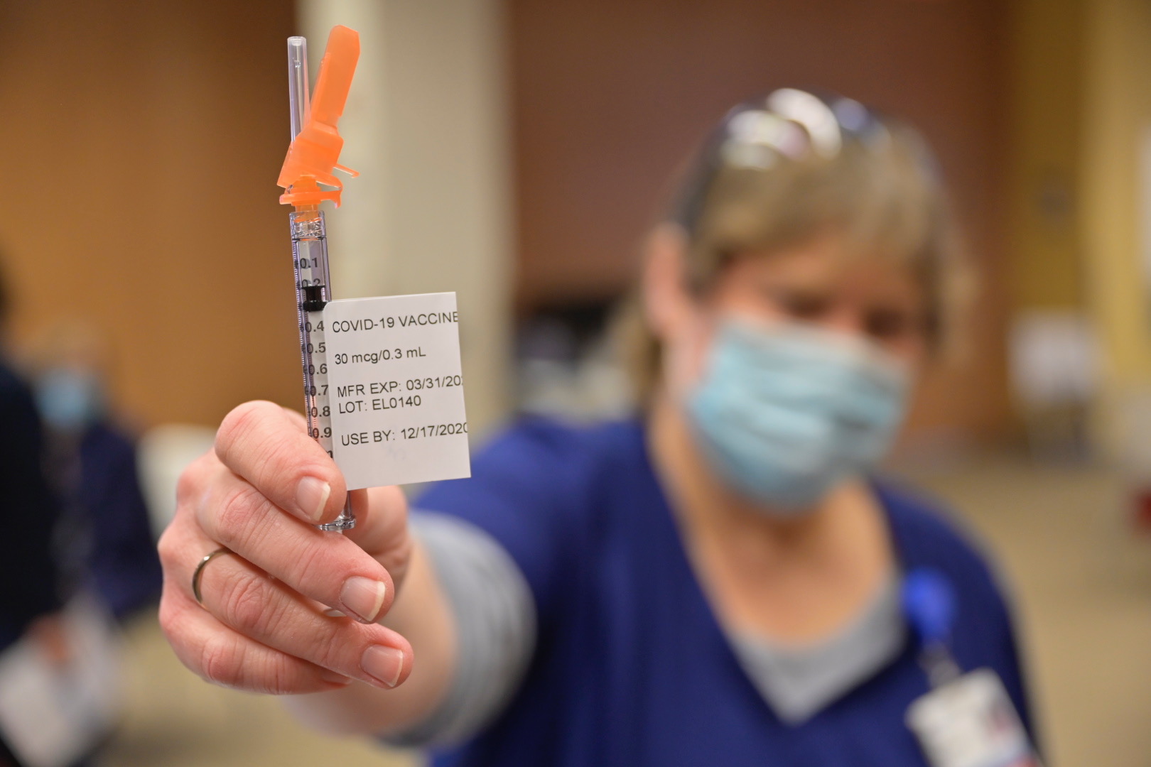 Masked medical personnel holding out a vial of COVID-19 vaccine.
