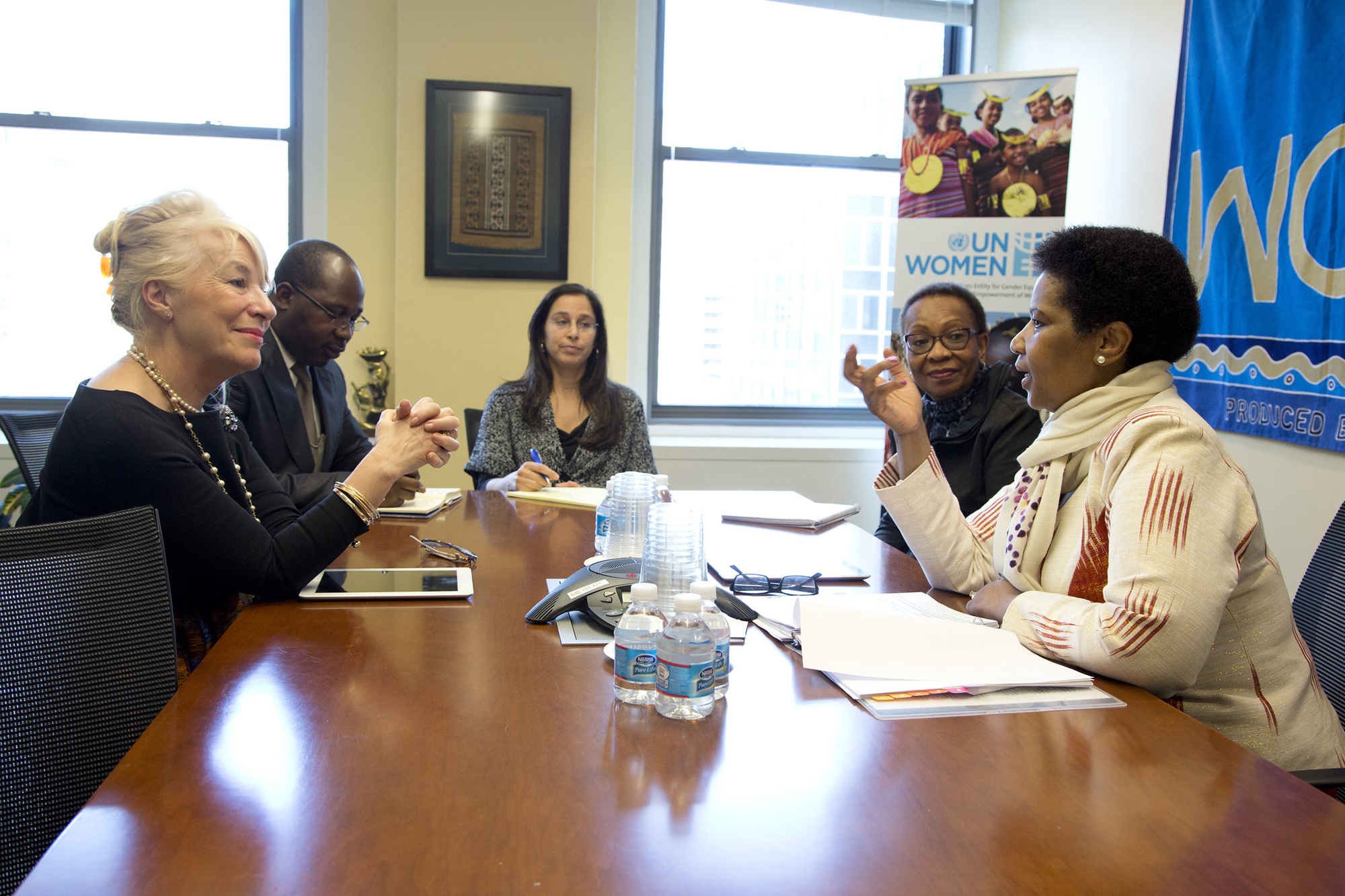 Five people sit together in a meeting; sign behind them reads "UN Women"