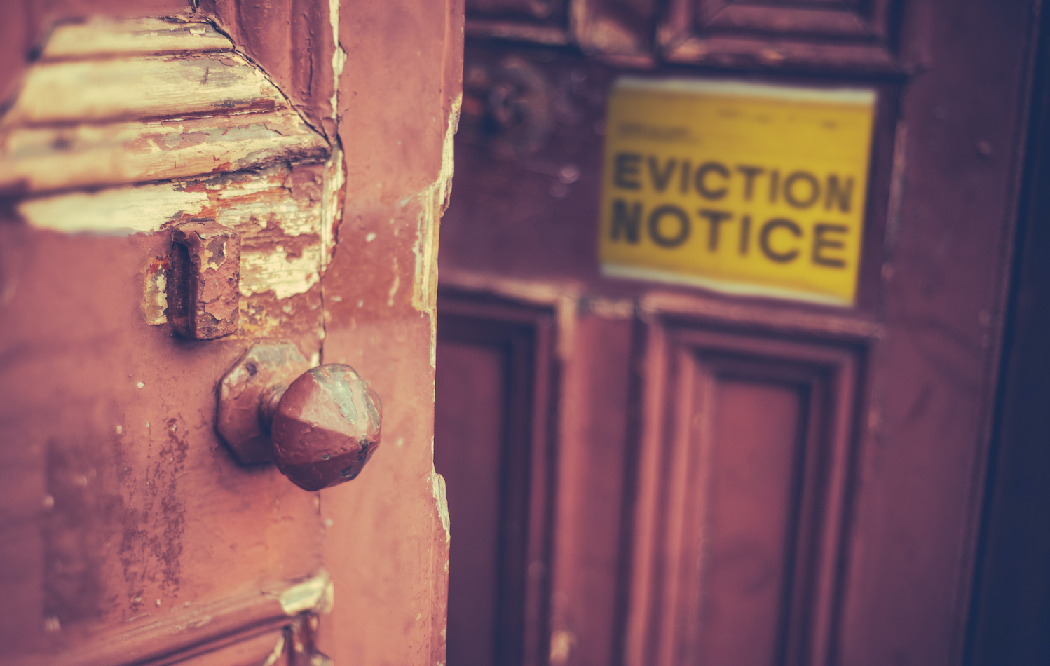 A close-up of an old chipping door. Blurred in the background is a sign that reads "EVICTION NOTICE" in all capital letters.