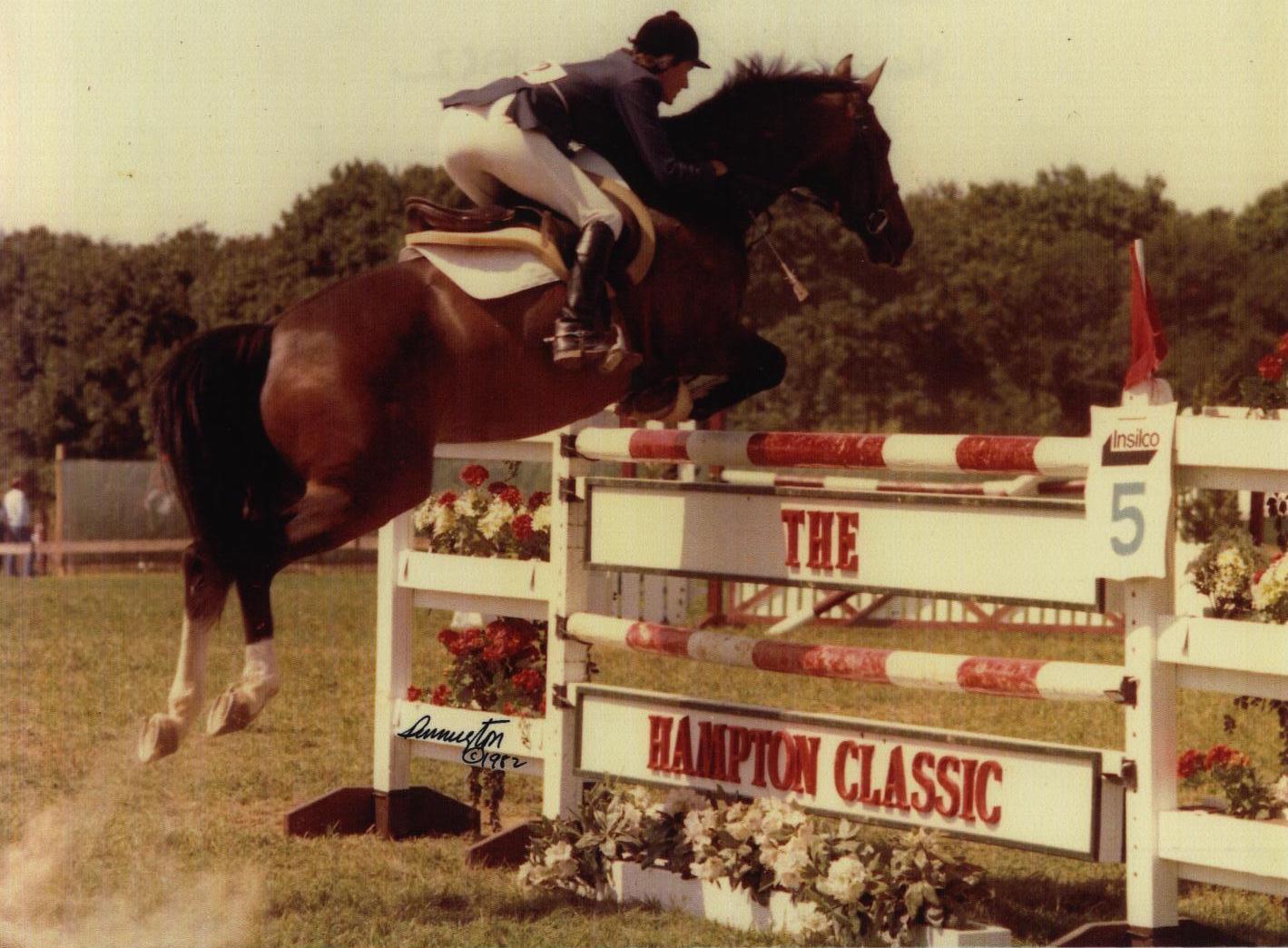 Older photo of equestrian on horse jumping over barrier that reads The Hampton Classic