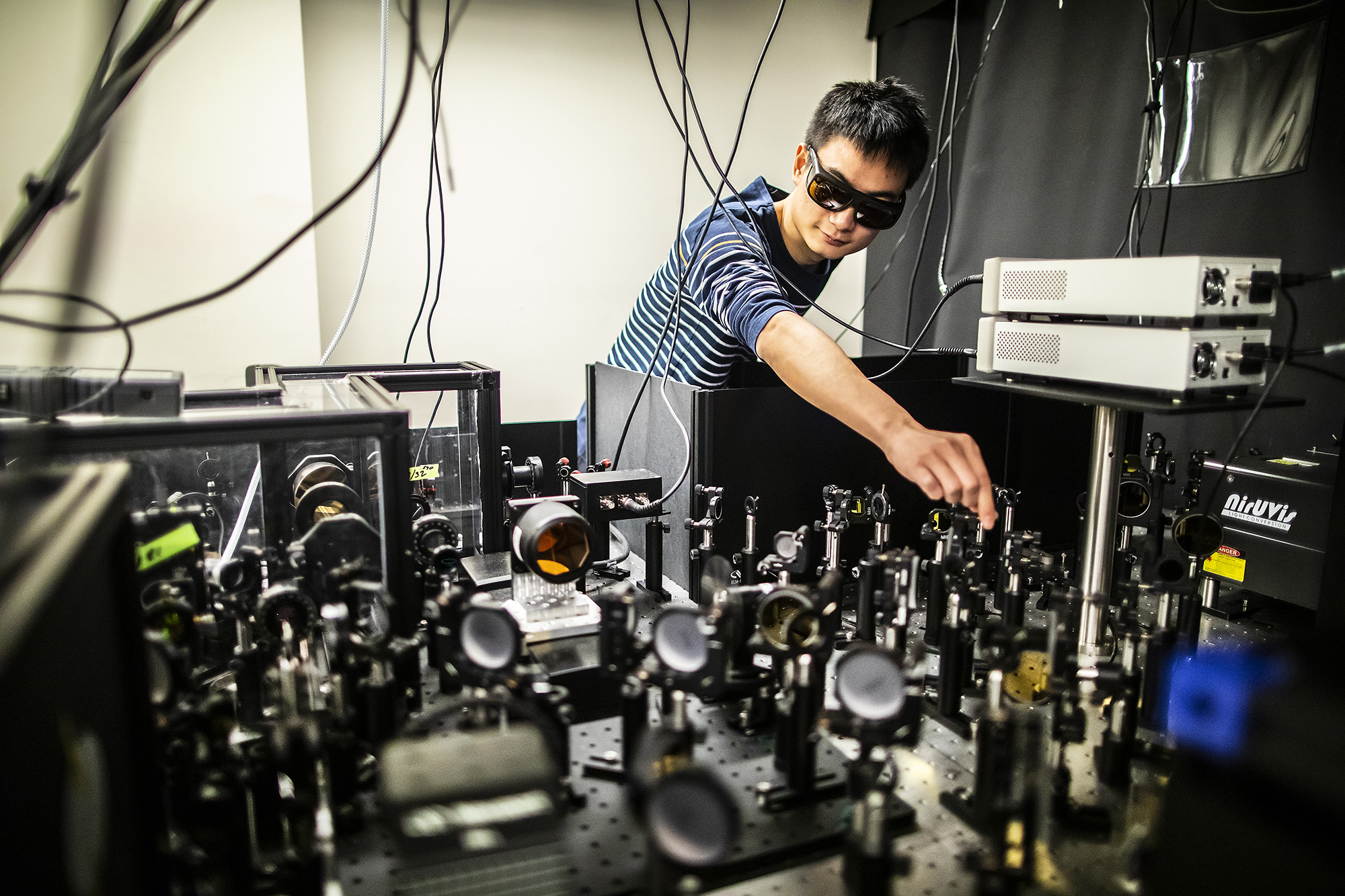 a person wearing darkened glasses adjusting lenses on an optics table