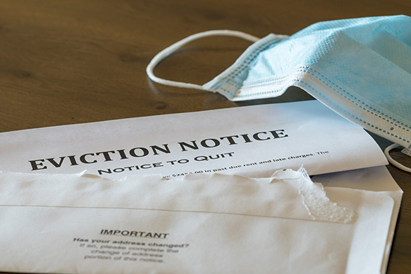 Opened envelope with an eviction notice inside on a table beside a discarded face mask.