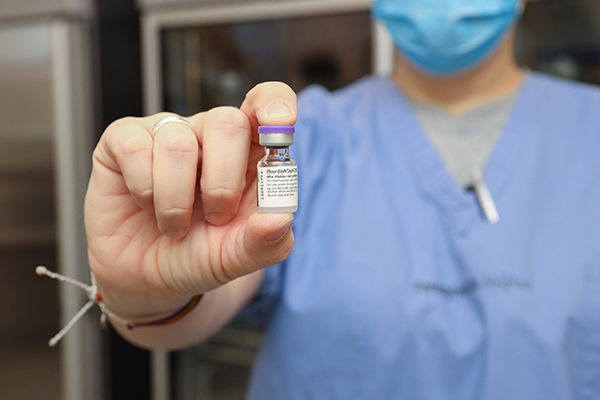 medical professional in scrubs holds a vial of covid vaccine.