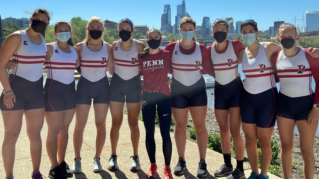 Members of the women's rowing team stand arm-in-arm along the Schuylkill River.