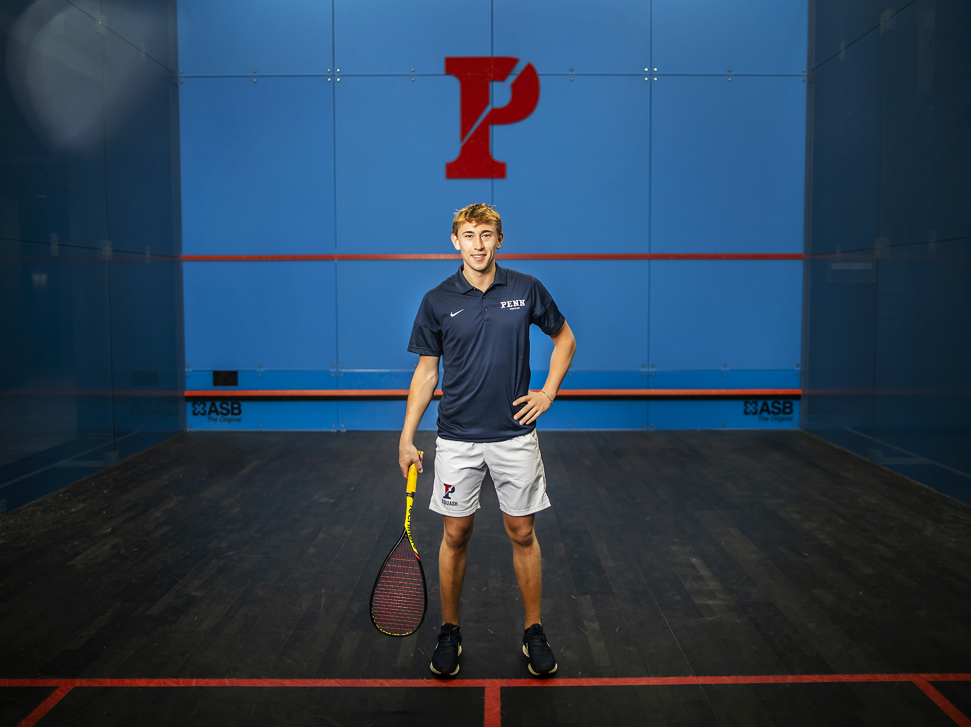 Andrew Douglas stands on the court at the Penn Squash Center with his racquet by his side.
