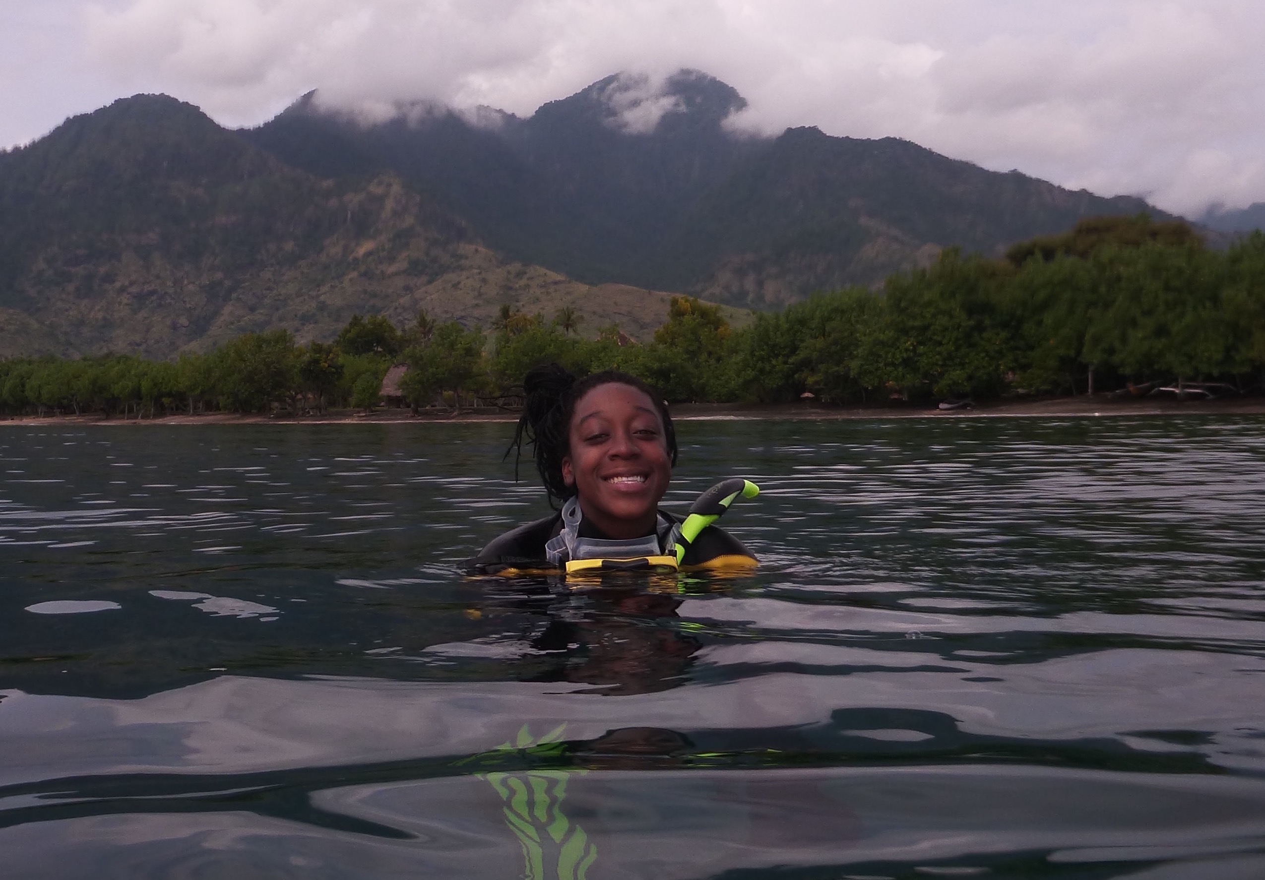 Camille Gaynus in scuba gear in the water with mountains in the background
