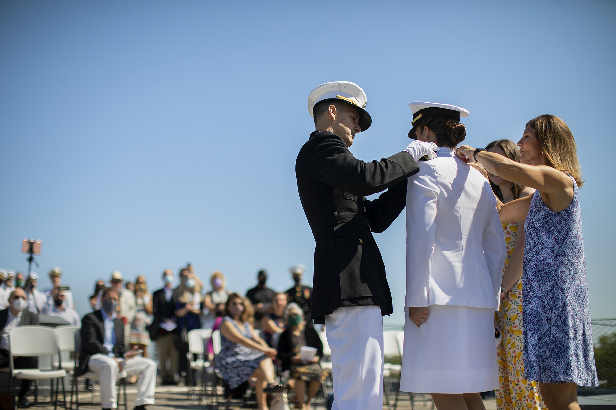 People aboard the USS New Jersey watch a midshipmen receive a medal by one person in uniform and a family member.