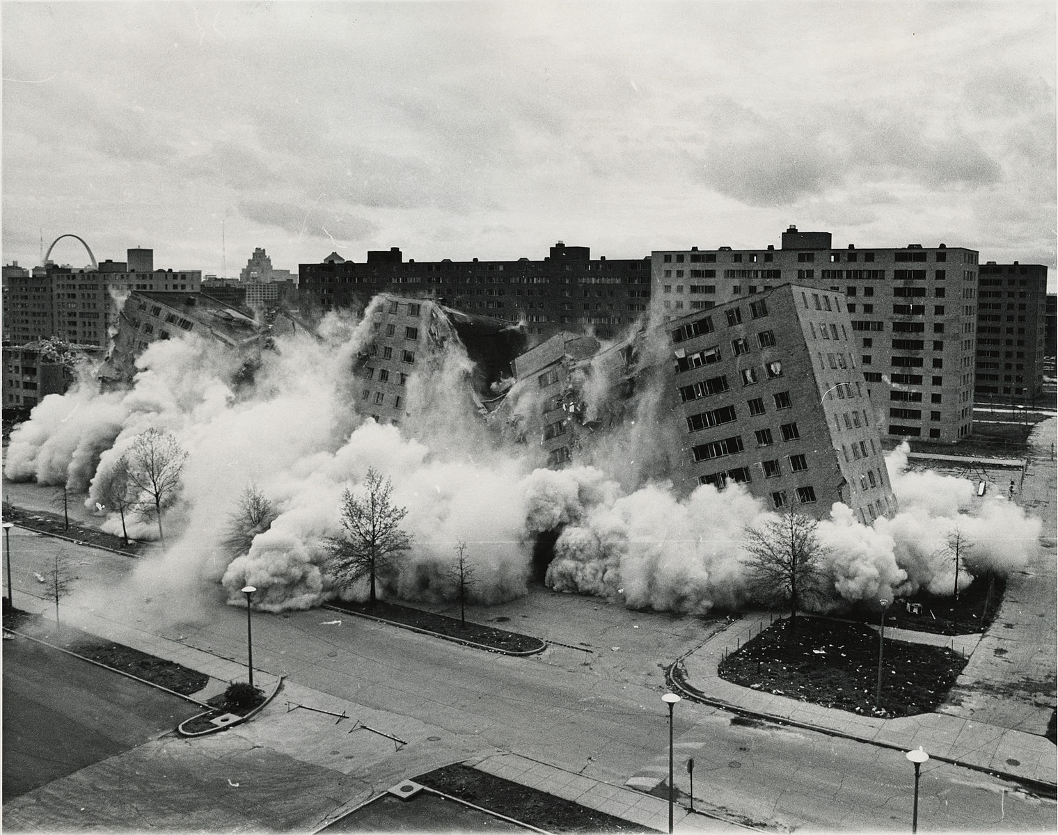 A black and white image of high-rise buildings collapsing in a cloud of dust