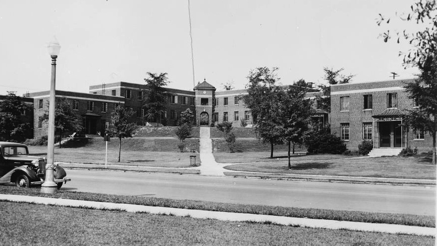 Black and white image of a two-story building with grass and trees in front