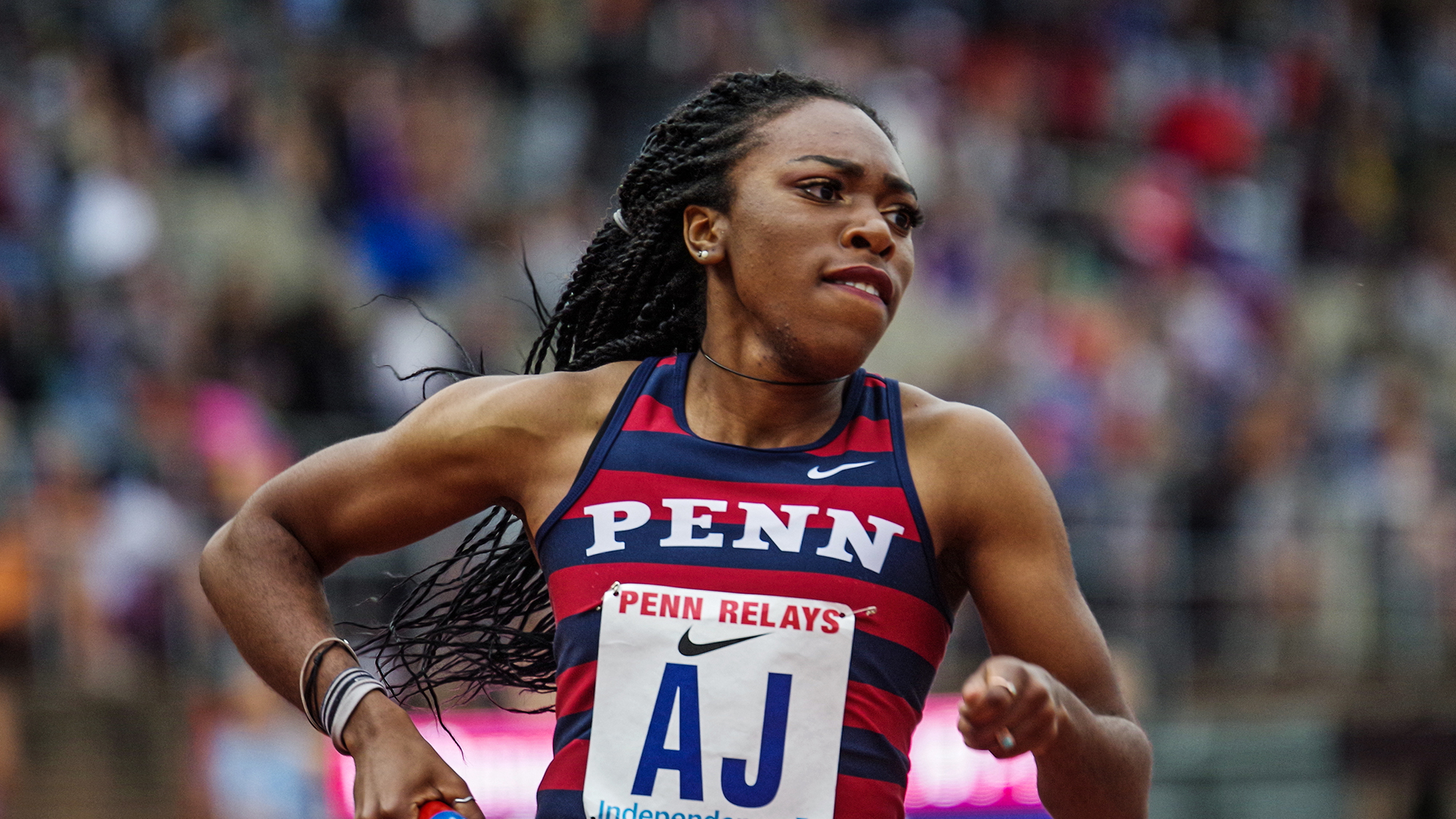 Uchechi Nwogwugwu runs a race during the Penn Relays while holding a baton.