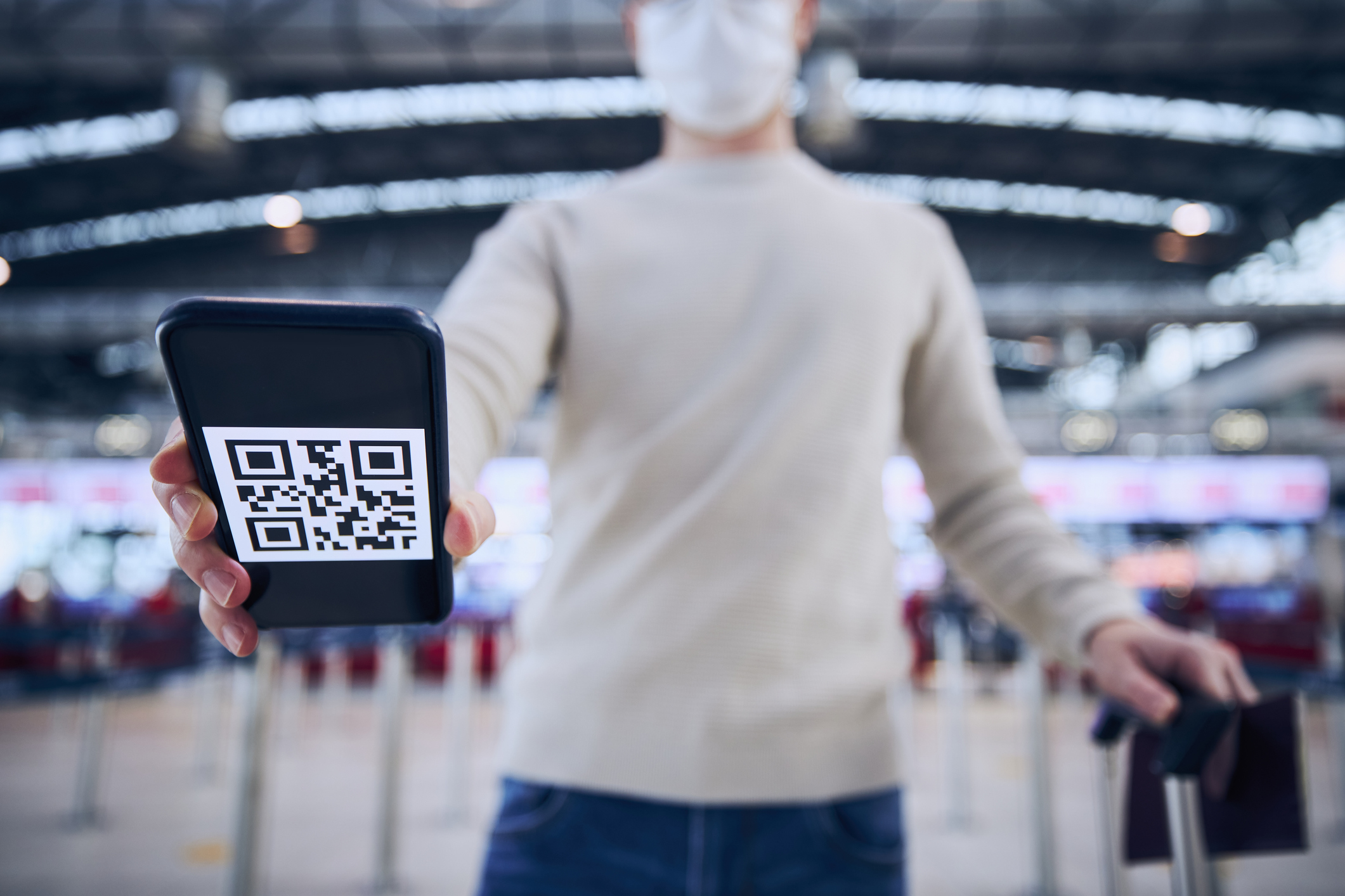 a person wearing a mask with a QR code on their phone scanning their ticket in an airport