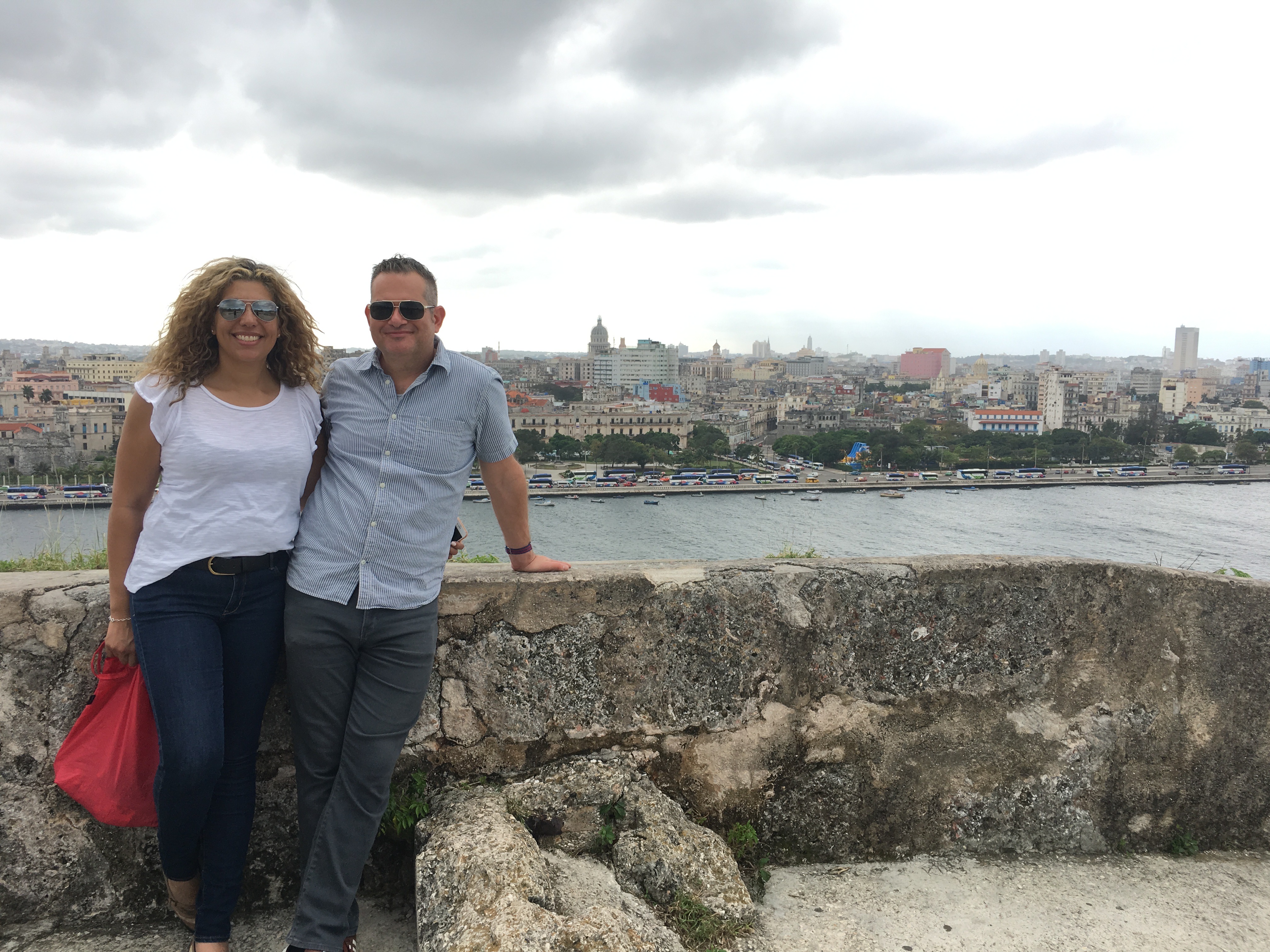 Two smiling people against a rock wall; water and city in background