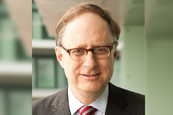 Man in suit with glasses and short hair wearing a suit and tie smiles into the camera