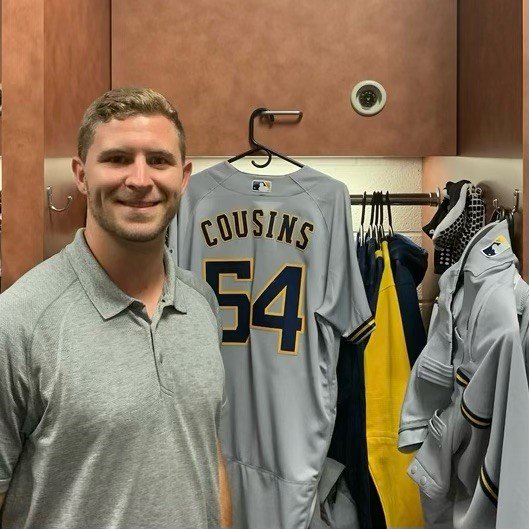 Jake Cousins stands at his locker next to his Brewers baseball jersey.