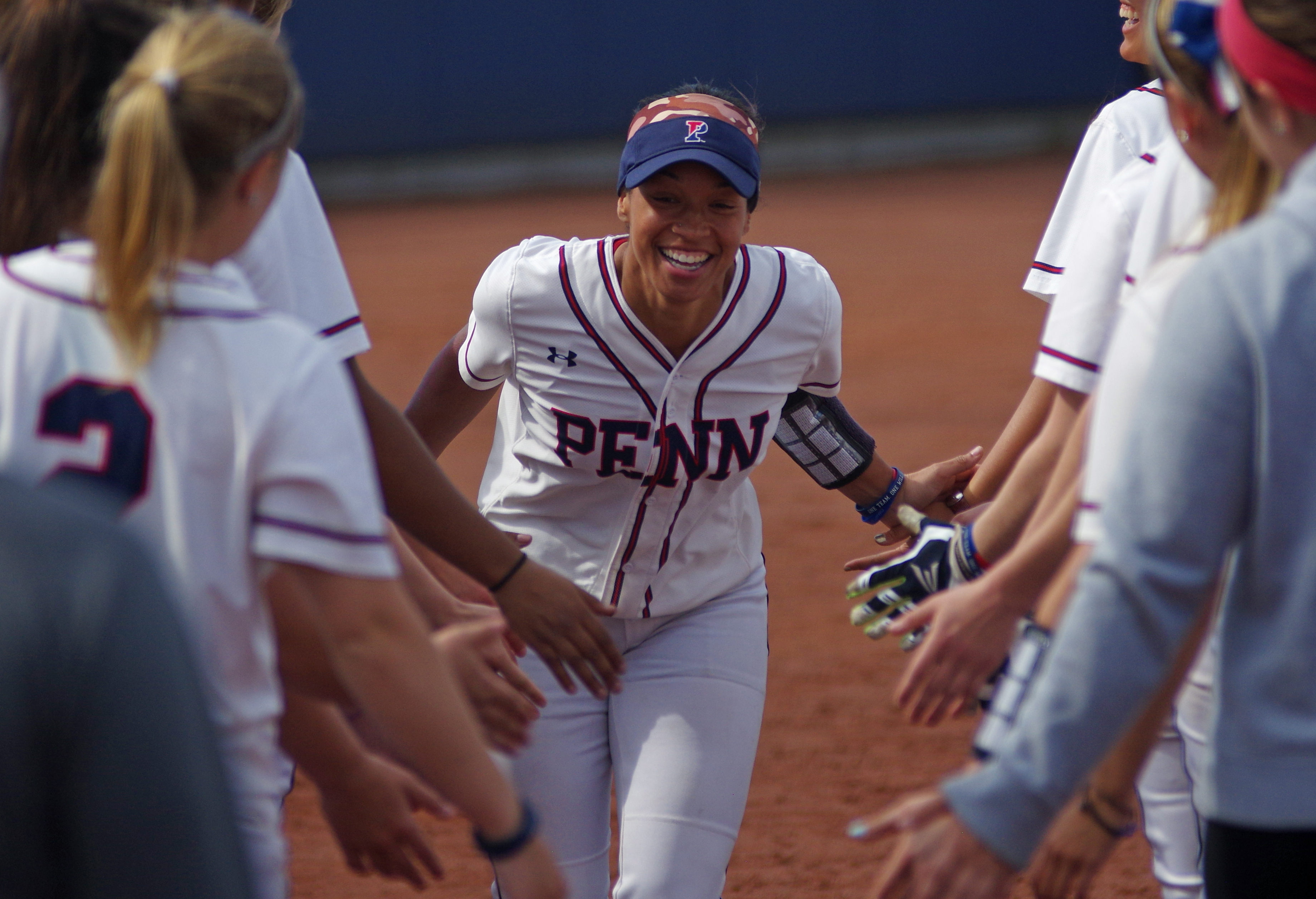 Penn softball player between two rows of other players slapping their hands