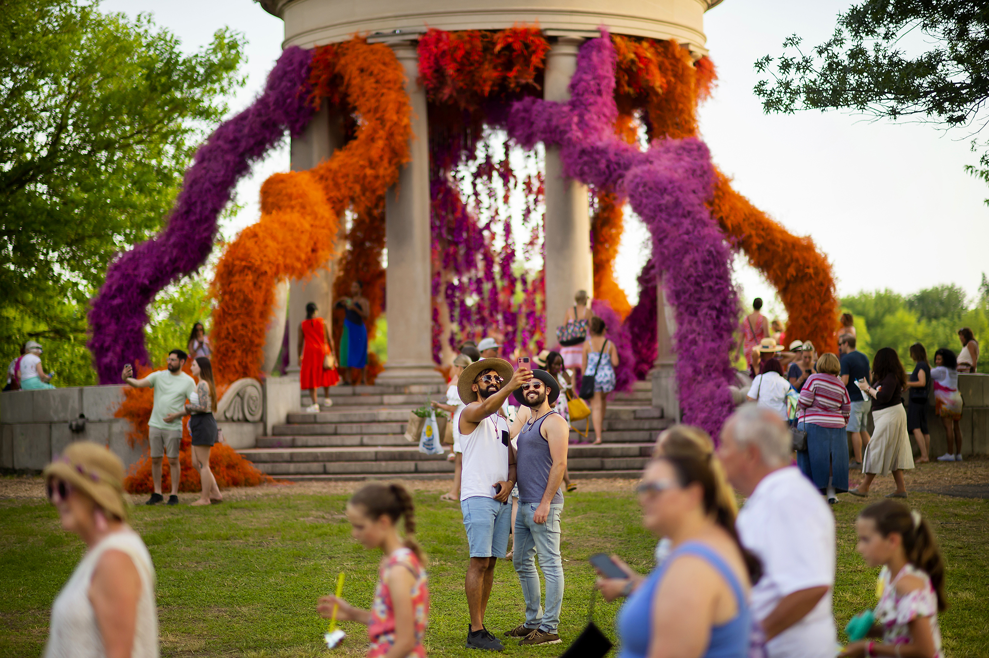 A gazebo with large strings of flowers jutting out, as onlookers take photos.
