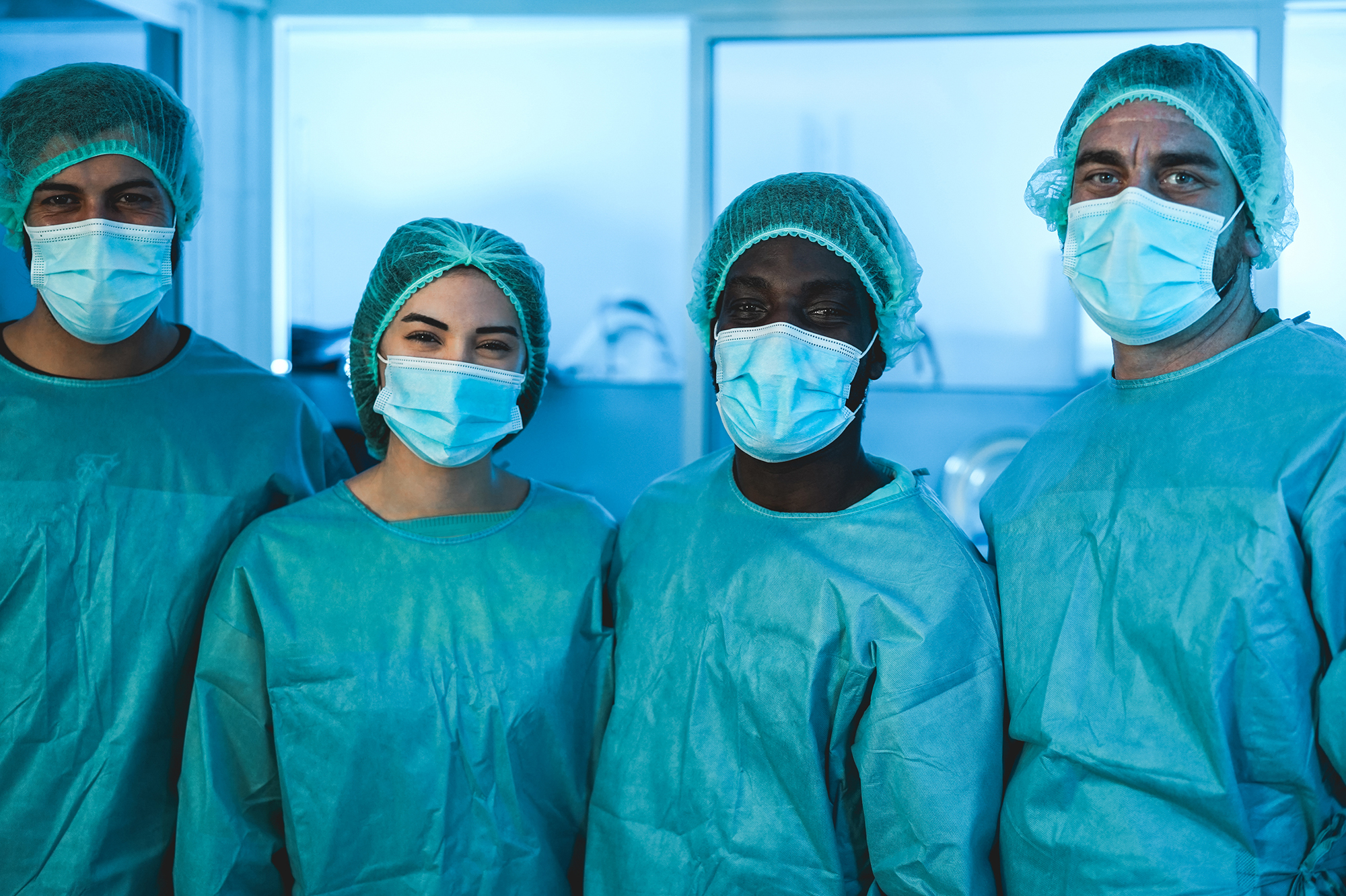 Four nurses in gowns and masks standing smiling in a row.
