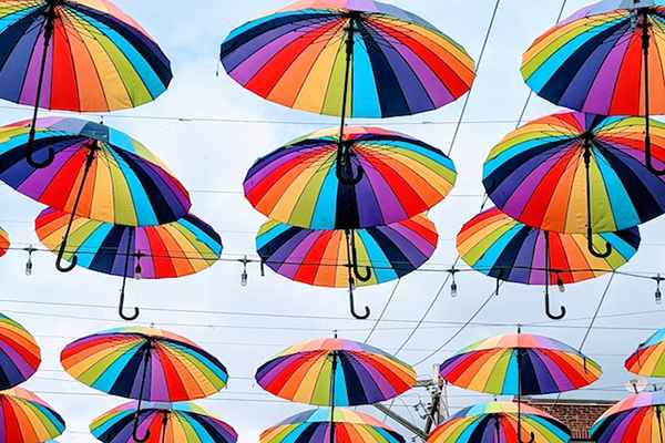 Many rainbow-colored umbrellas hanging from overhead strung lighting.