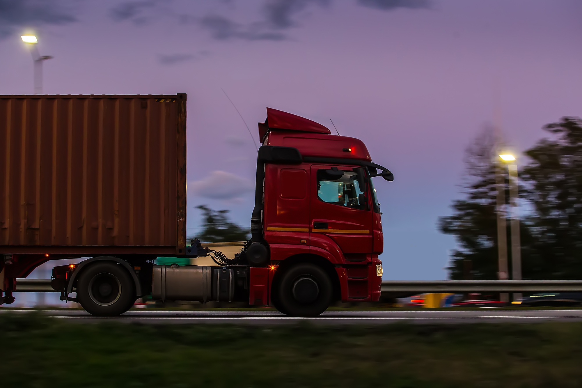 Eighteen-wheeler truck driving on the highway at dusk.