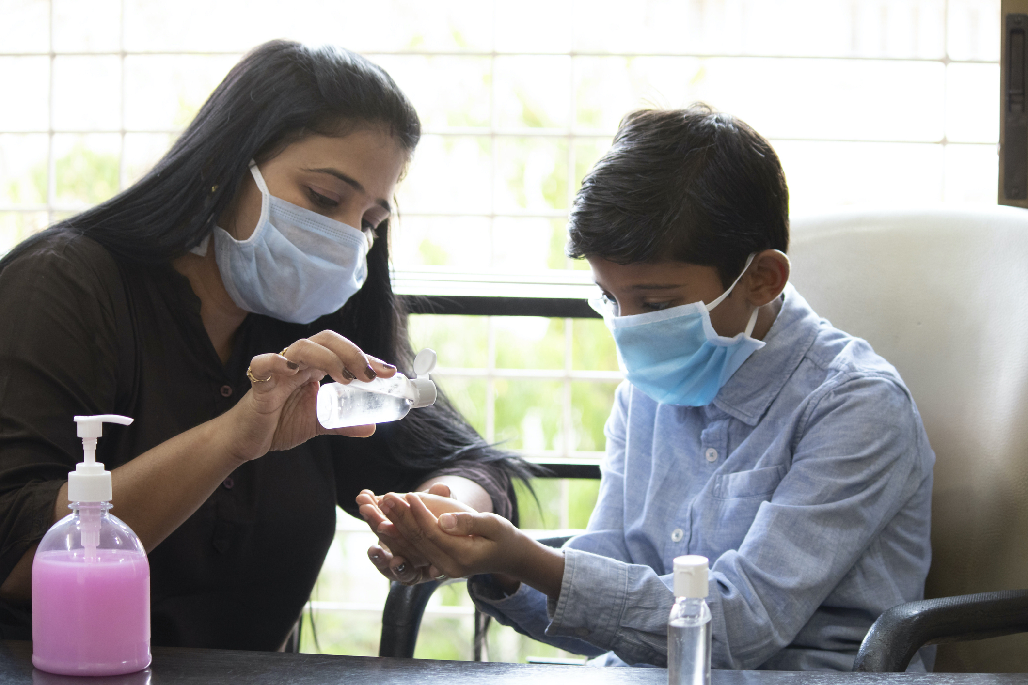 A person in a face mask giving hand sanitizer to a child also wearing a face mask.