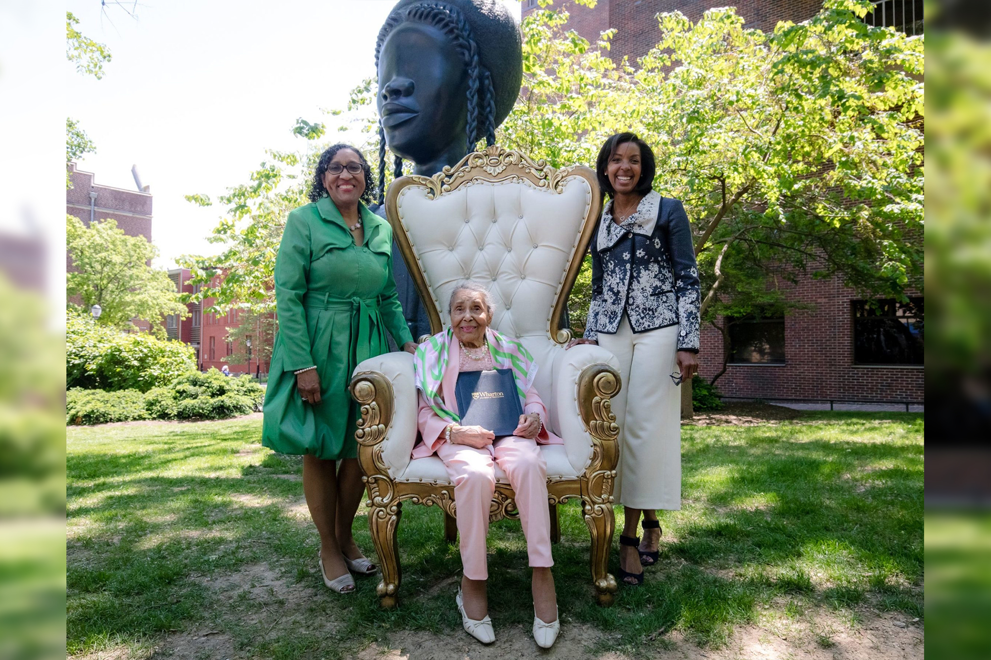 Hettie Simmons Love sits on a large ornate chair with daughter Karen Love standing to her left and Wharton Dean Erika James at her right in front of the Brick House statue.