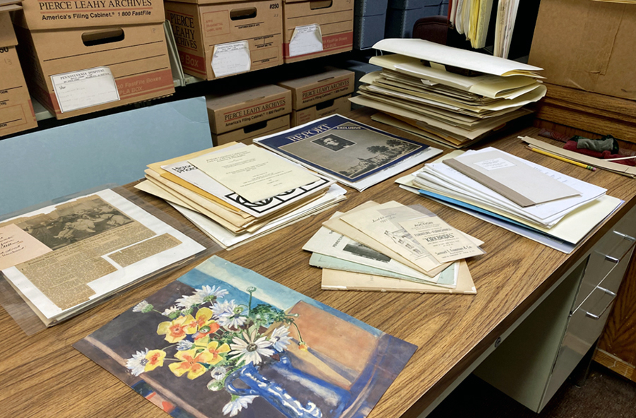A table in the archives office with an old painting, historic newspaper clippings, and old pamphlets from Penn Medicine archives.