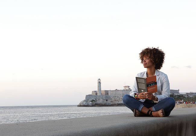 Amalia Dache sitting criss-cross applesauce on a sea wall in Cuba reading a book.