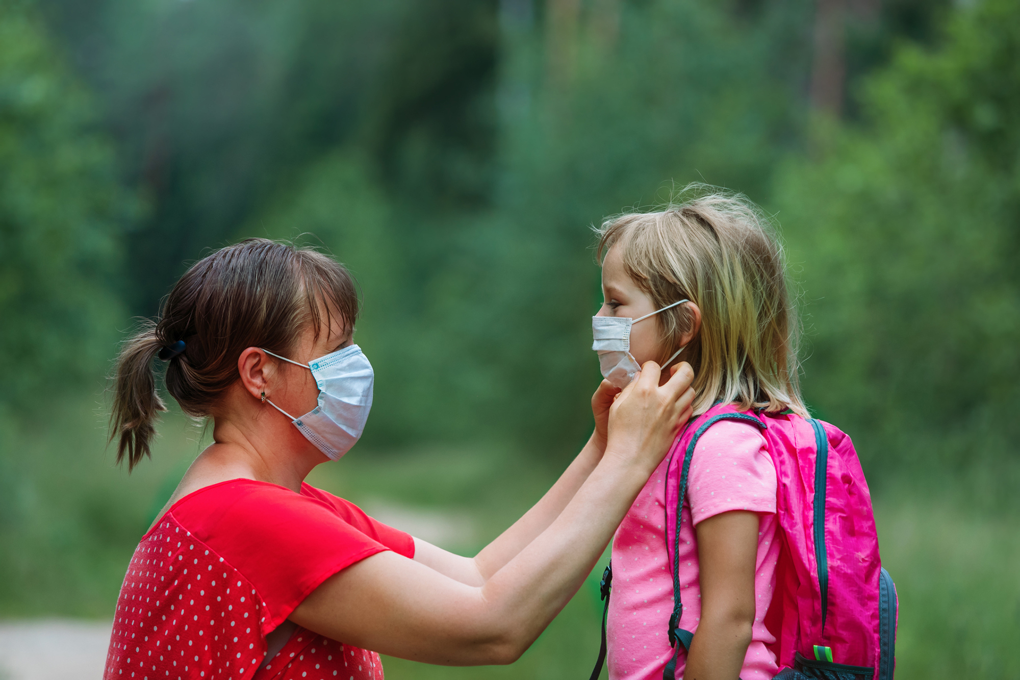 Adult wearing mask adjusts the mask of a young child