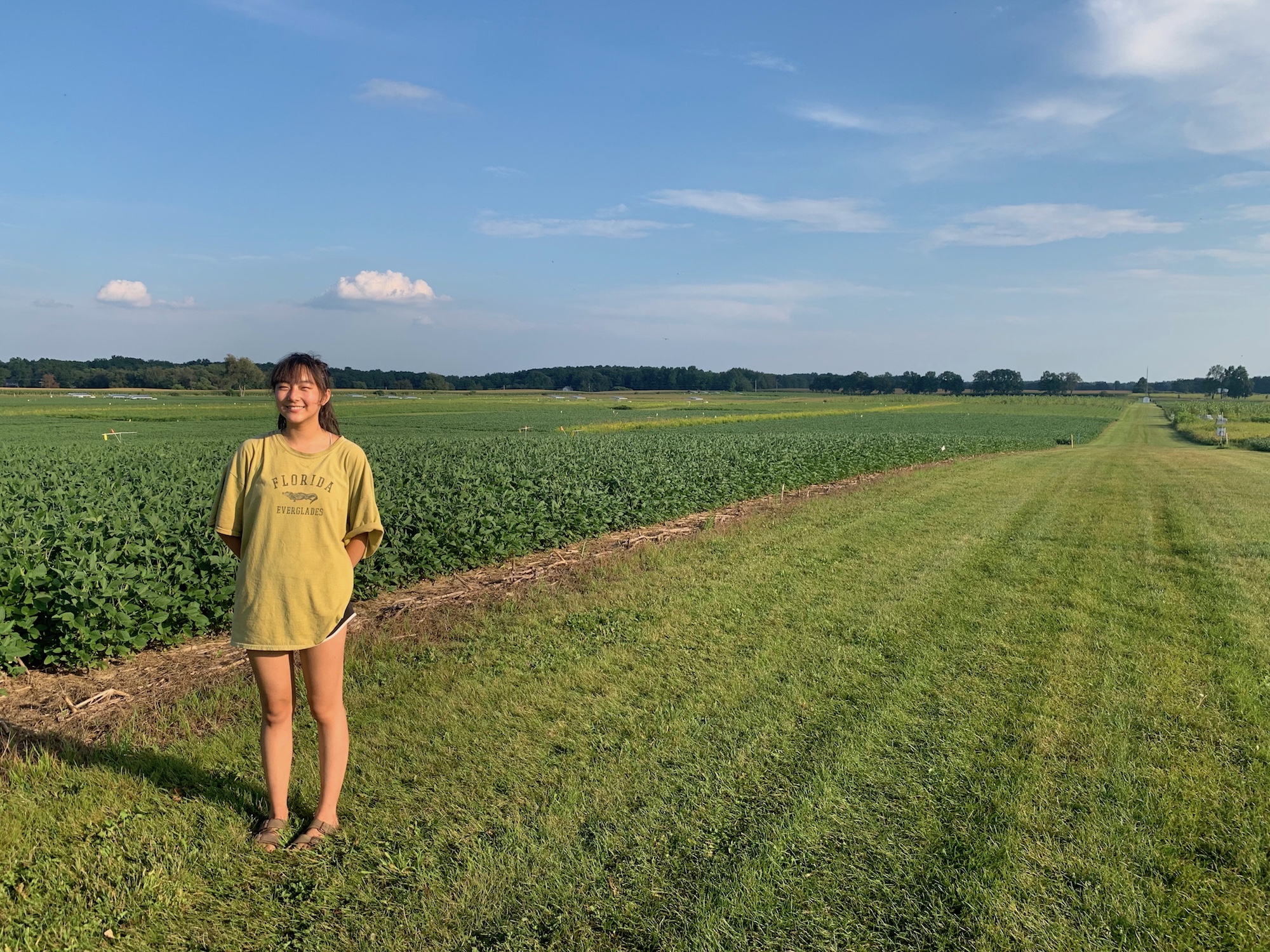Student Linda Wu smiles next to a field of soybeans