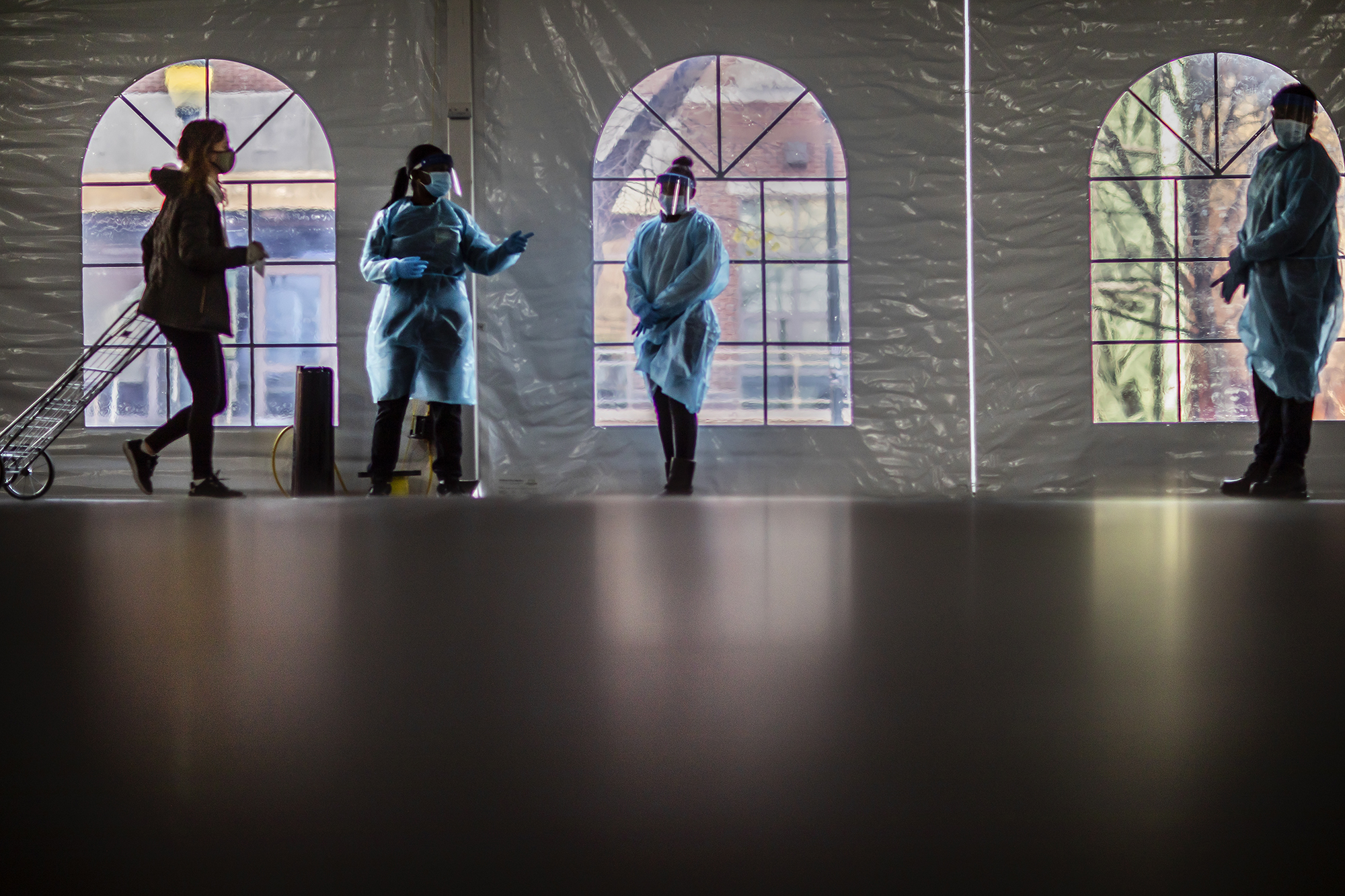 three people wearing personal protective equipment directing another person inside of a large plastic tent