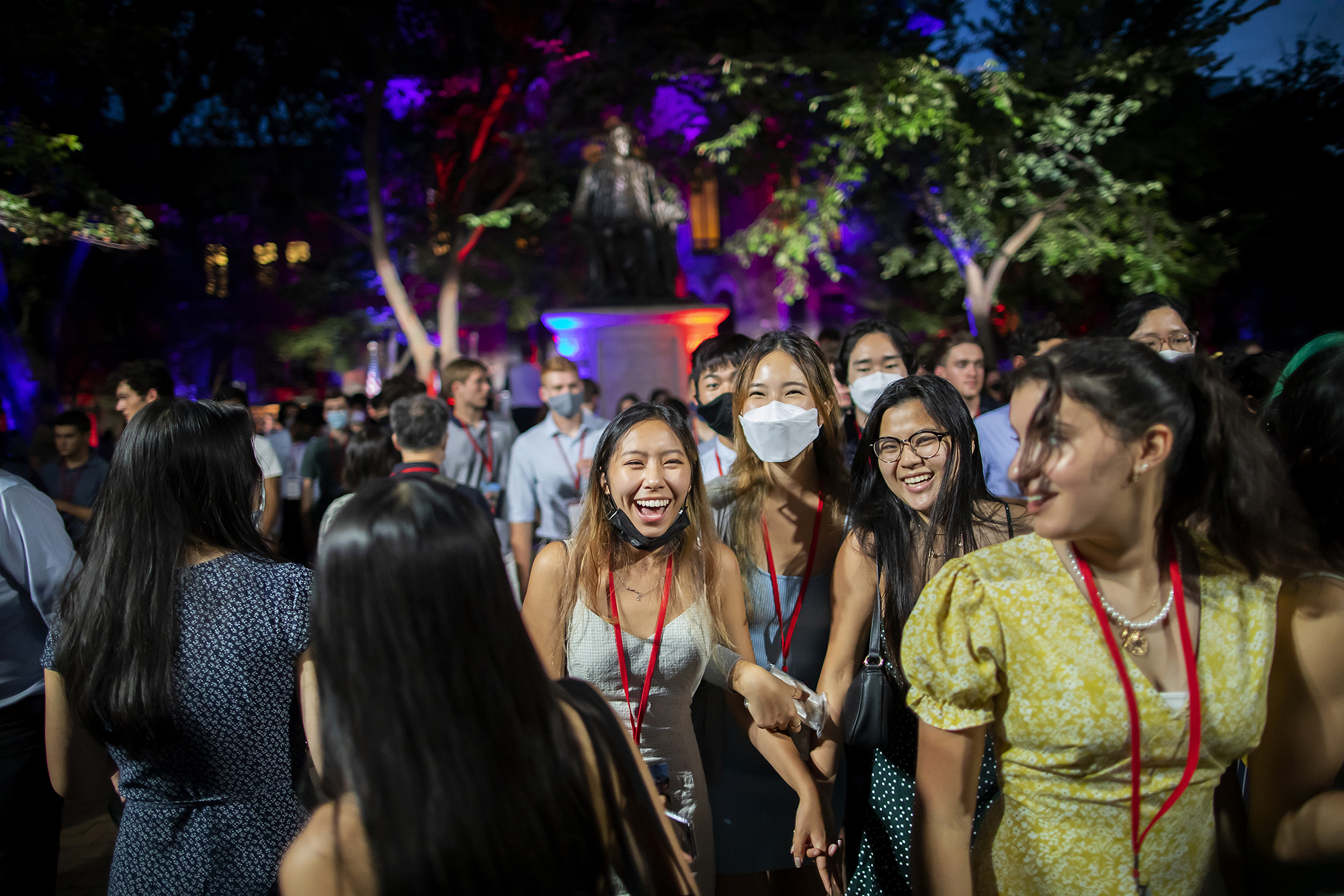 Students laugh and smile standing on College Green at night during Convocation.