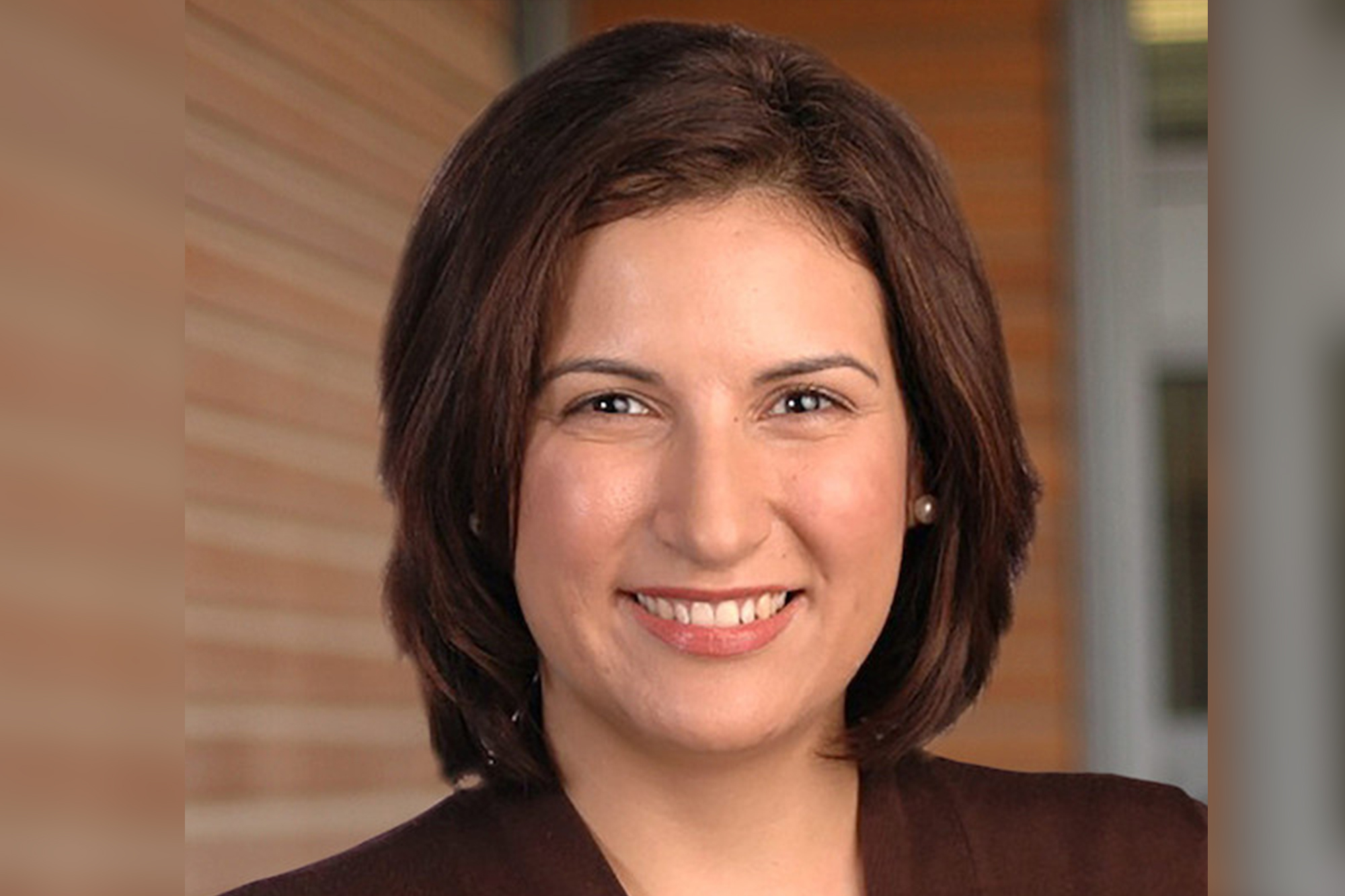 Woman with brown hair, pearl earrings and brown blazer smiles into the camera