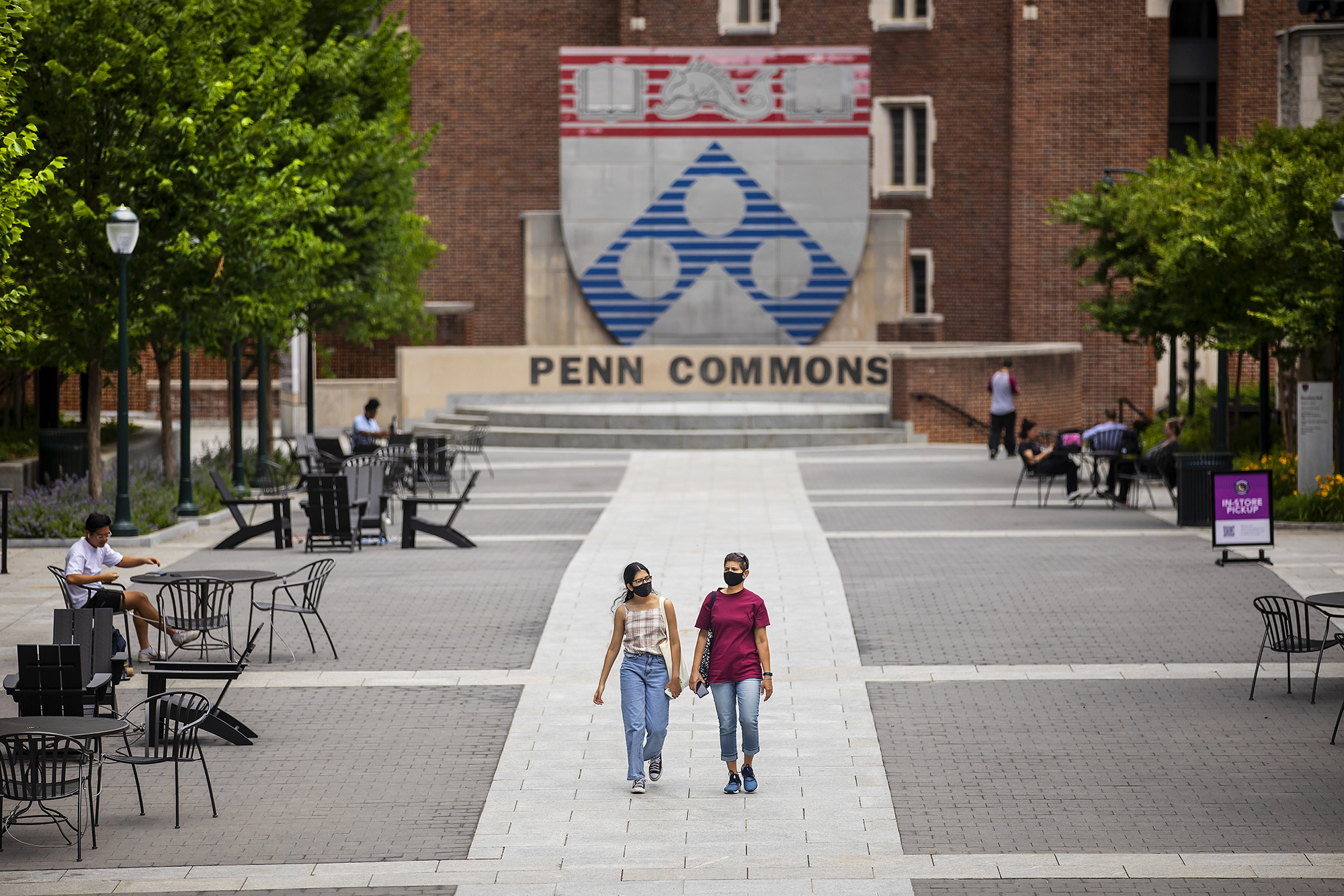 Two masked students walking through Penn Commons.
