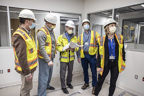 Five people wearing masks, hard hats and safety vests explore a new unit in the Penn Medicine Pavilion.