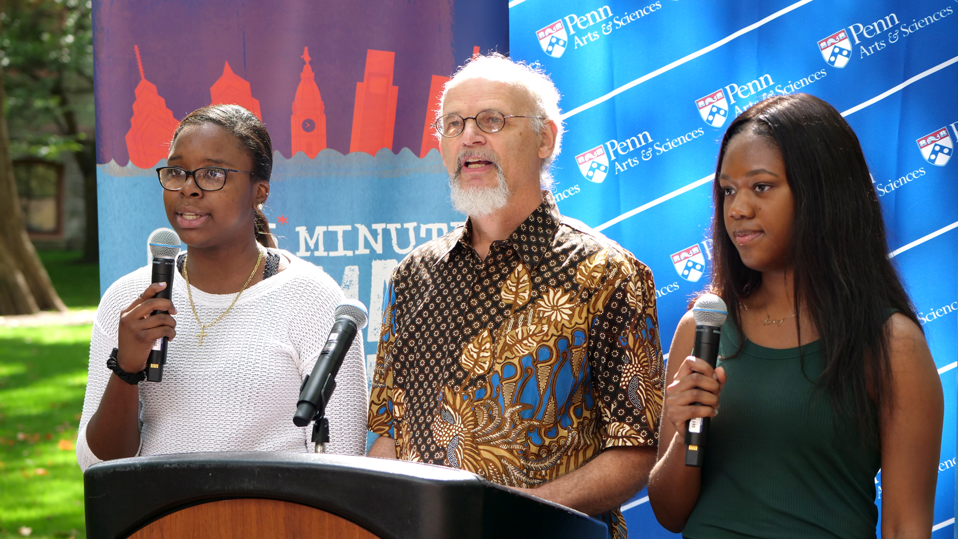 Three people speak at a lecturn outside