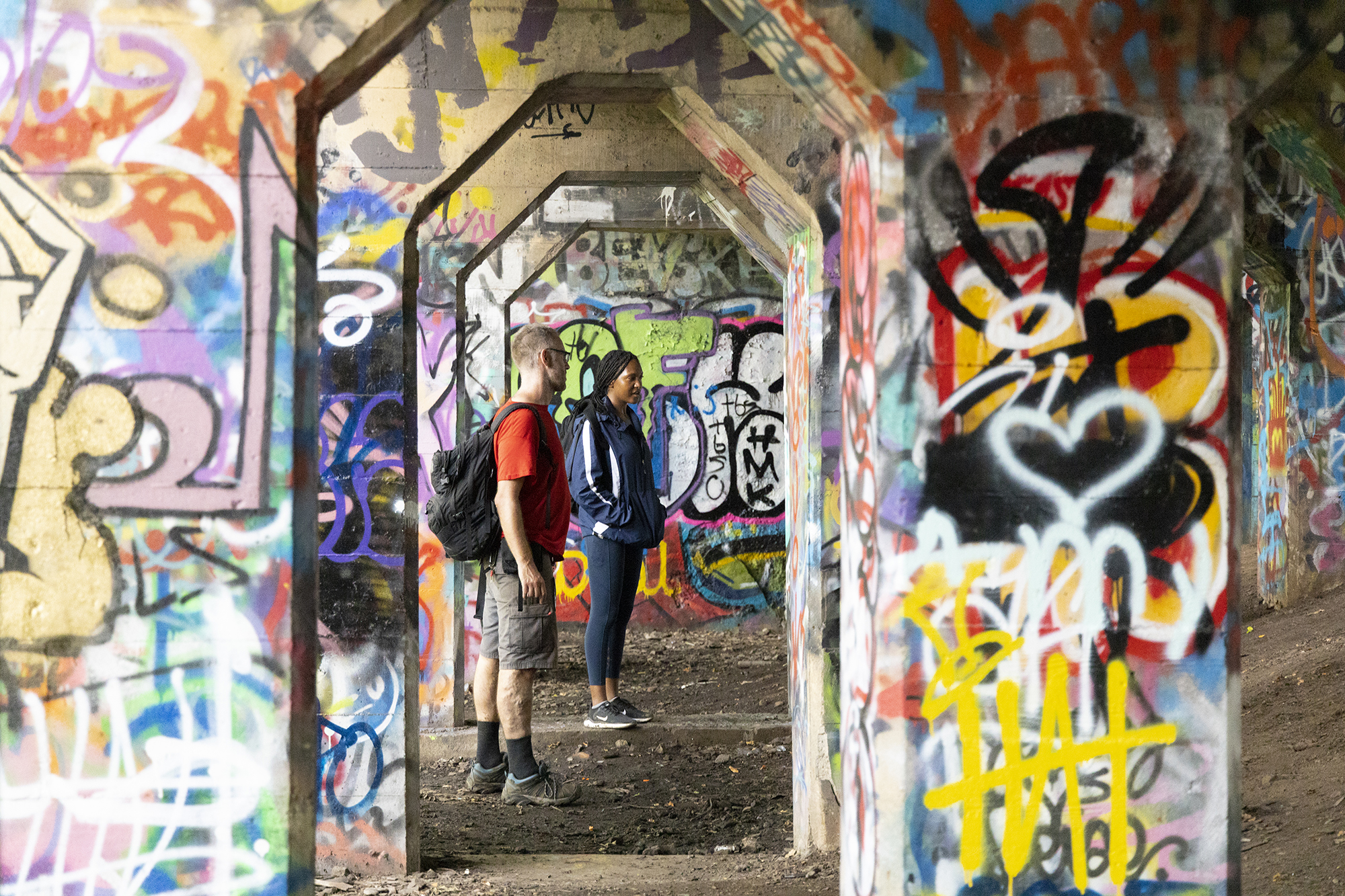 Two students stand among heavily graffitied underpass pillars in Philadelphia’s Graffiti Pier.