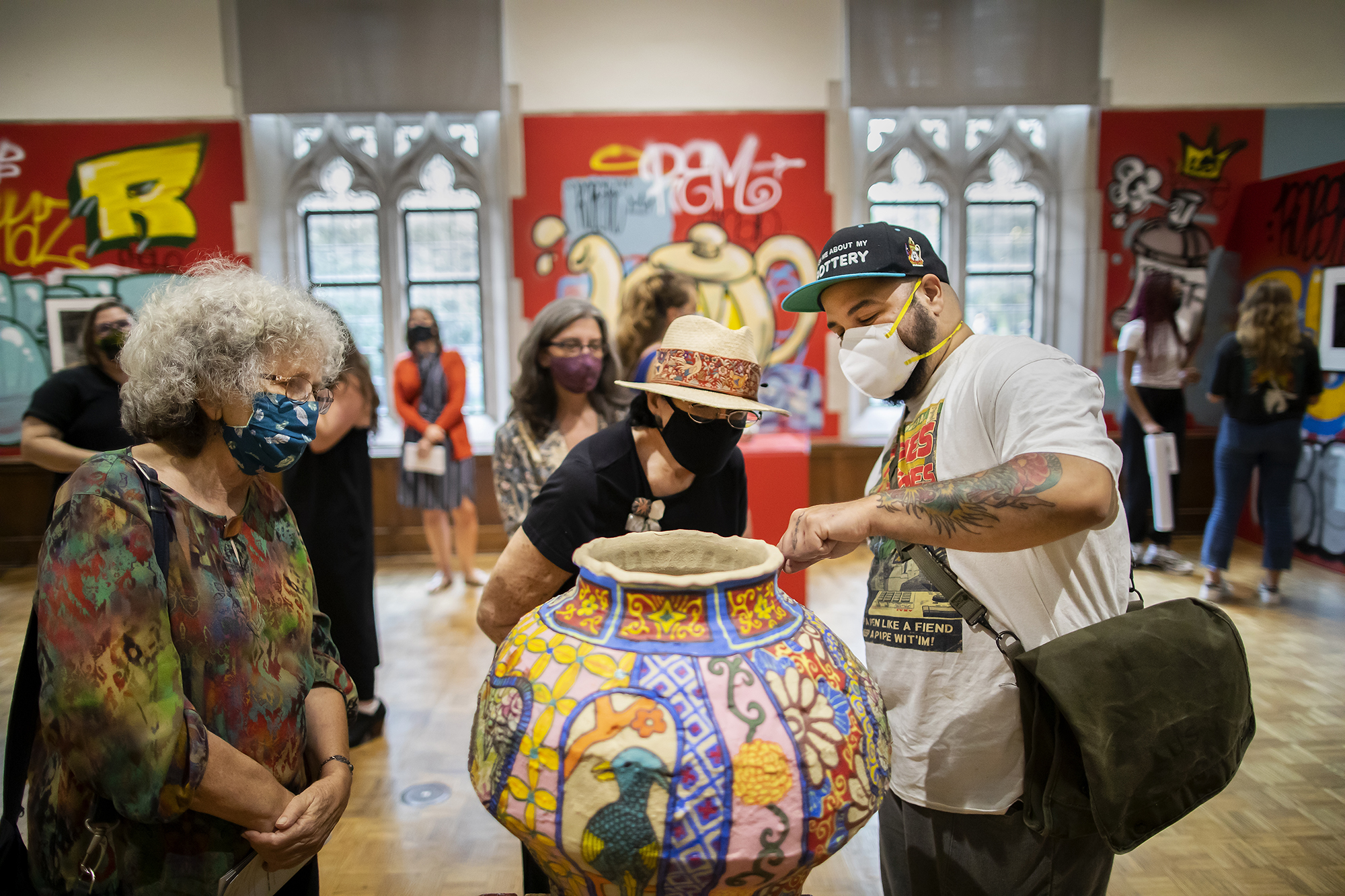 Artist pointing to painted ceramic pot while two people look and listen