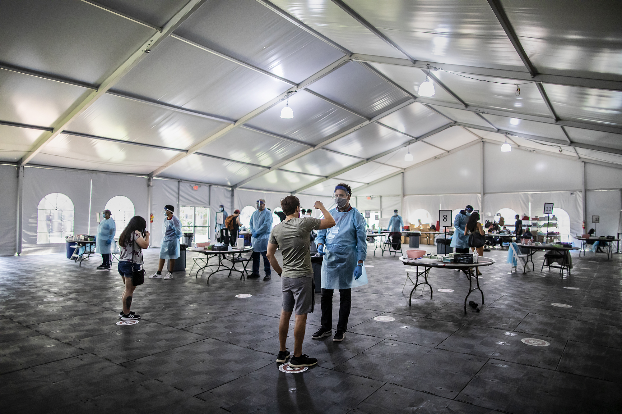 people in a large open tent taking saliva covid tests