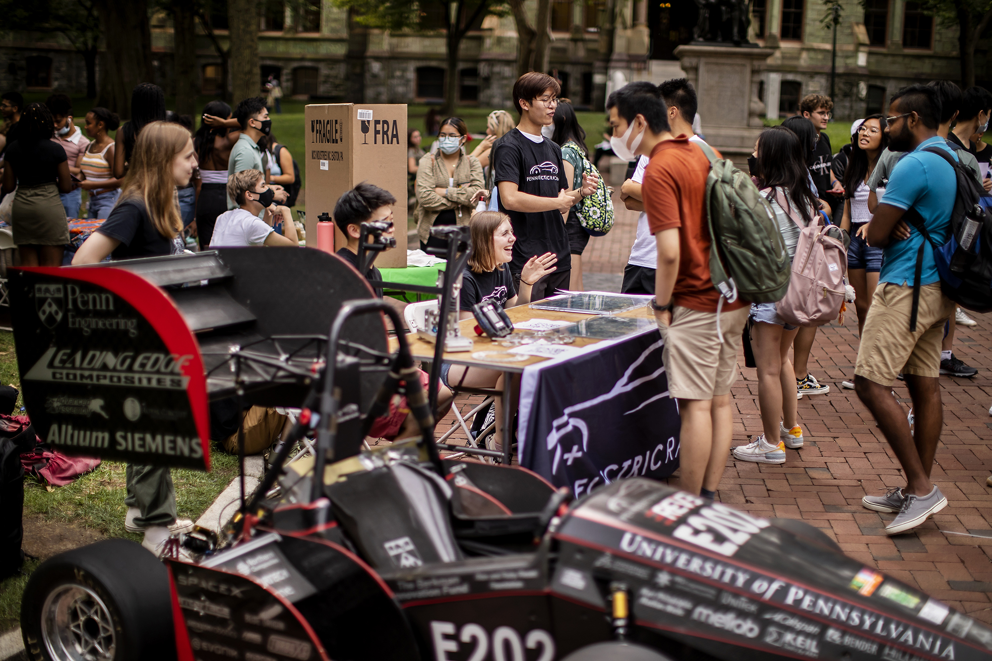 students outside at a table next to a racecar