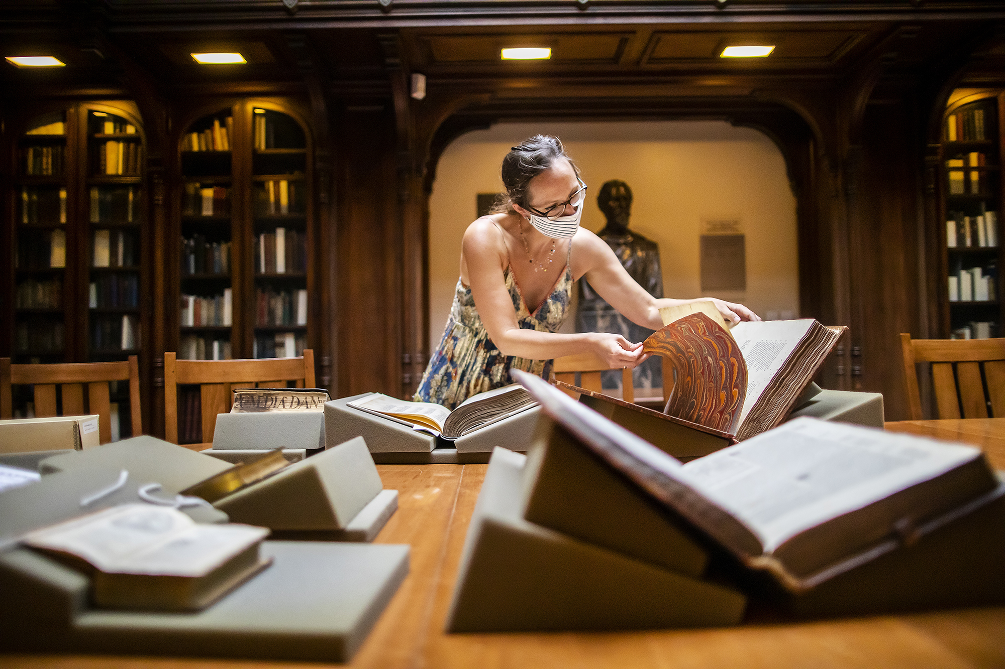 Woman pages through book. Many other books lie propped open on the table in front of her