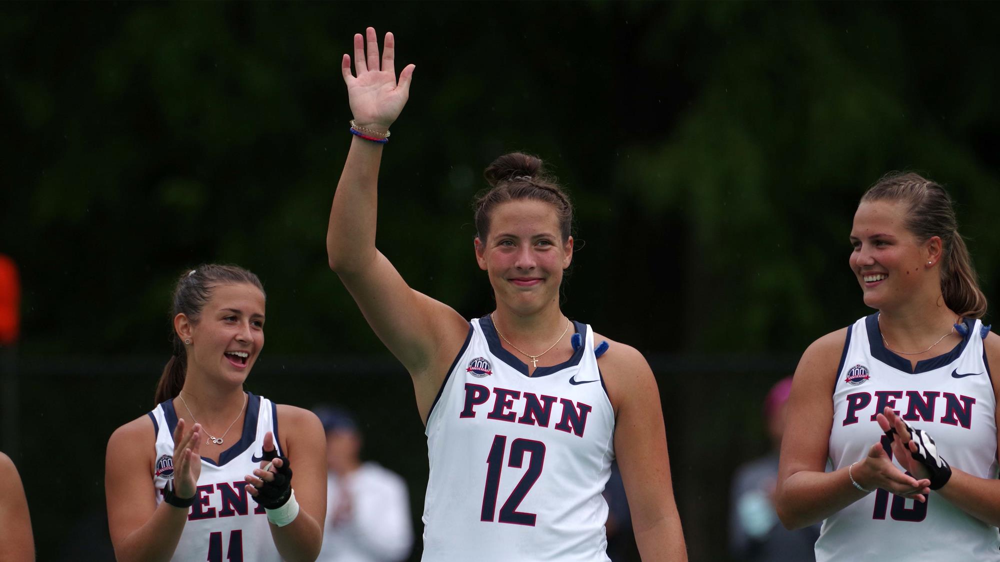 Banks raises her right hand while two teammates on each side clap.