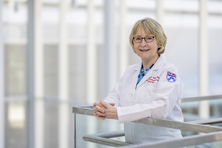 Deborah Culley standing by a railing at the Perelman School of Medicine in a white lab coat.