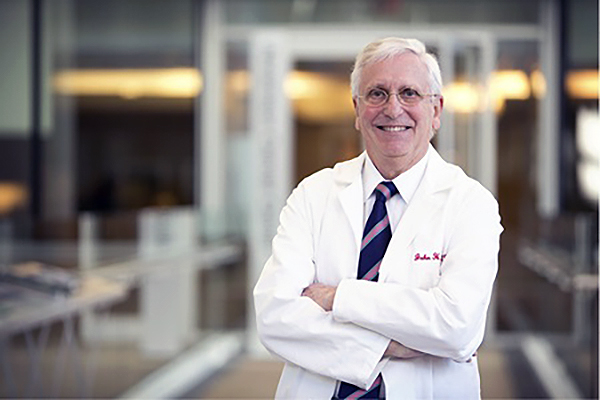 John Glick standing with arms crossed in a white lab coat.