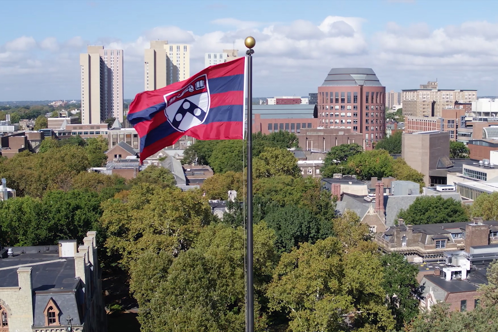 University of Pennsylvania flag flying with campus and the city of Philadelphia in the background.