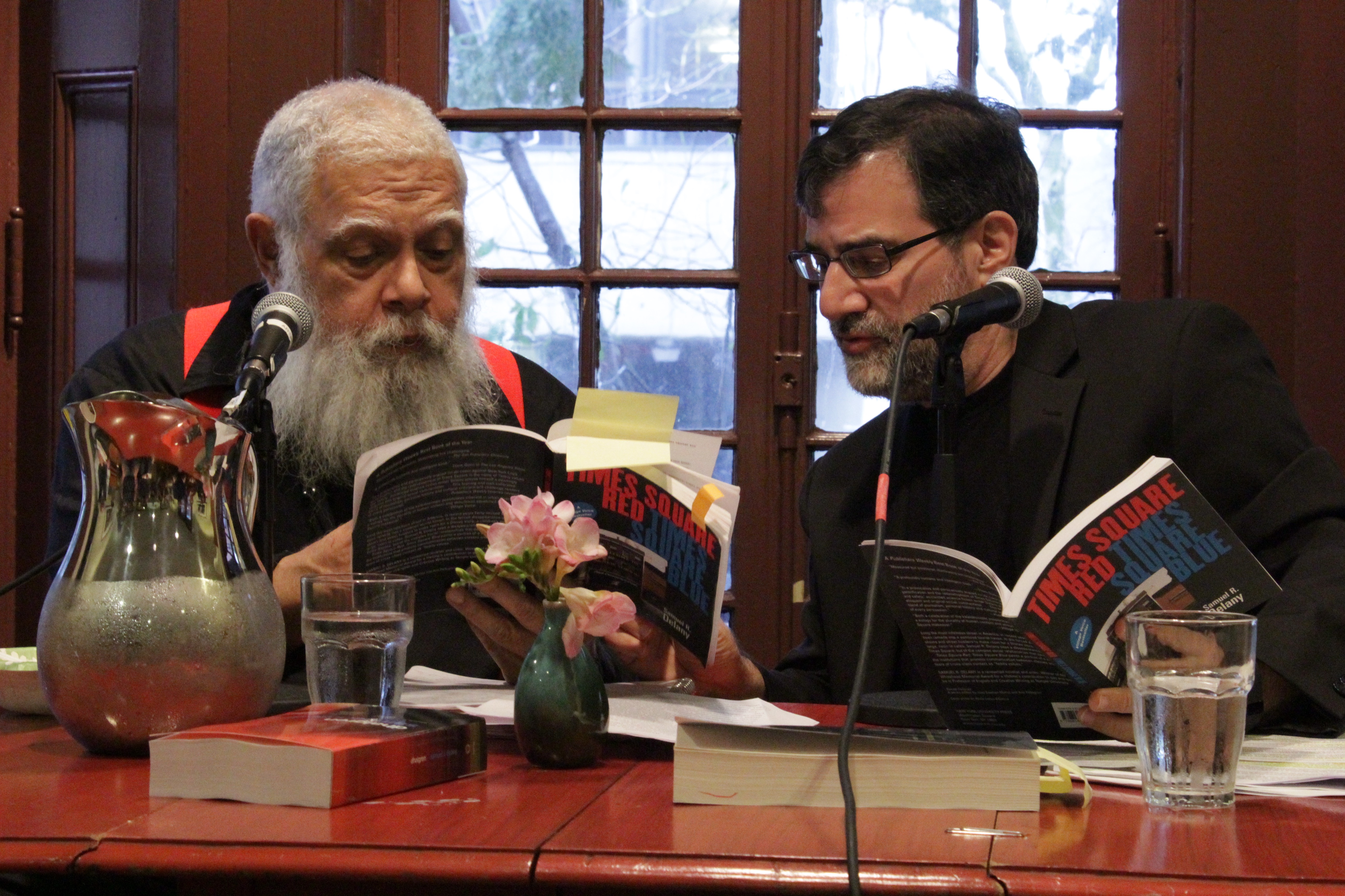 Samuel Delany and Al Filreis sit at a table looking at two copies of the same book.