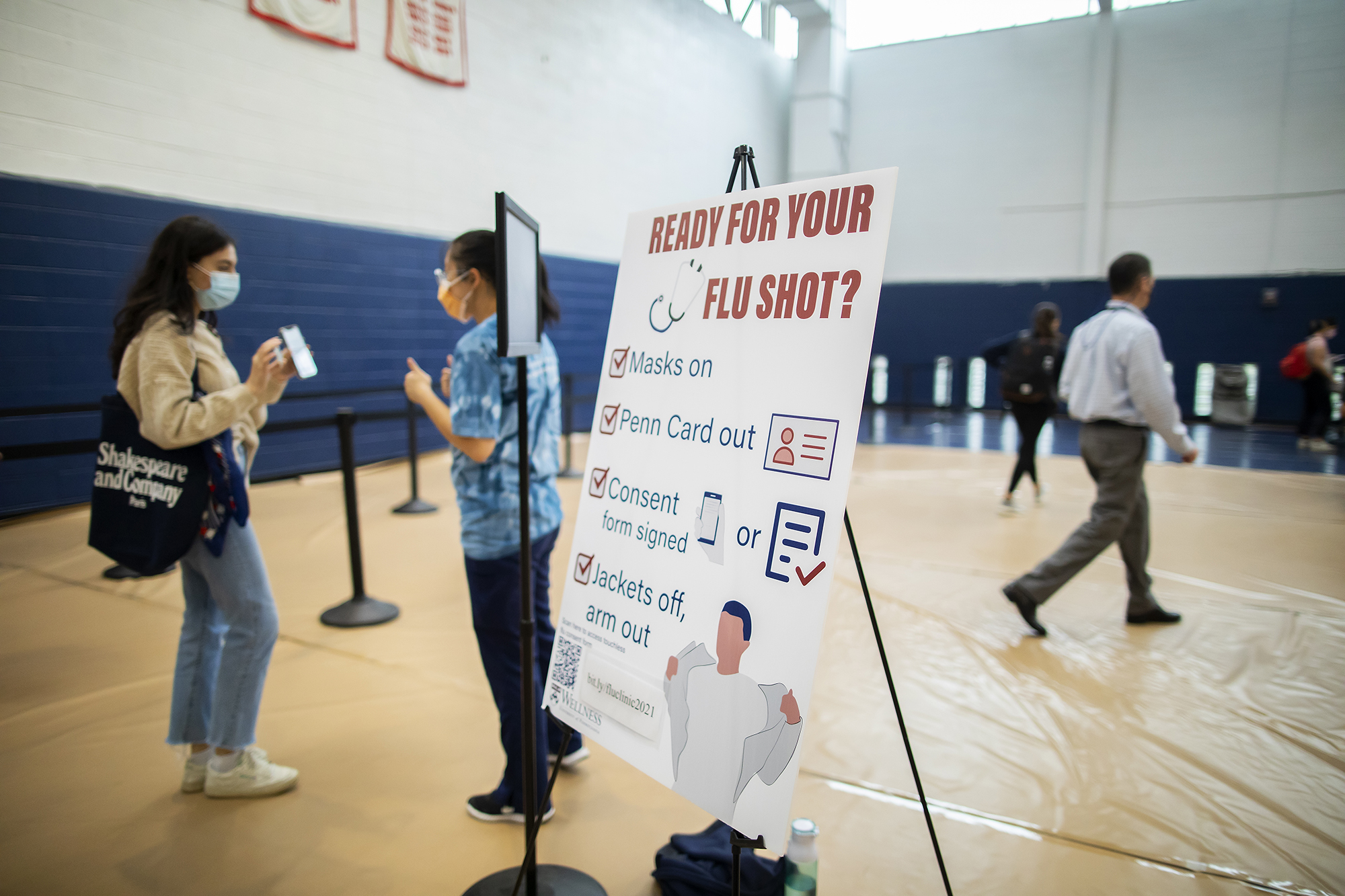 A patient checks in at a flu vaccine clinic next to a sign that says "Ready for your flu shot?"