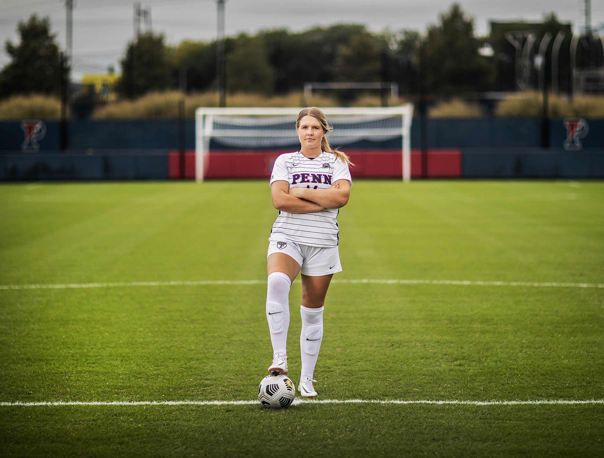 Mia Shenk stands on Rhodes Field with her foot on a ball and her arms folded.