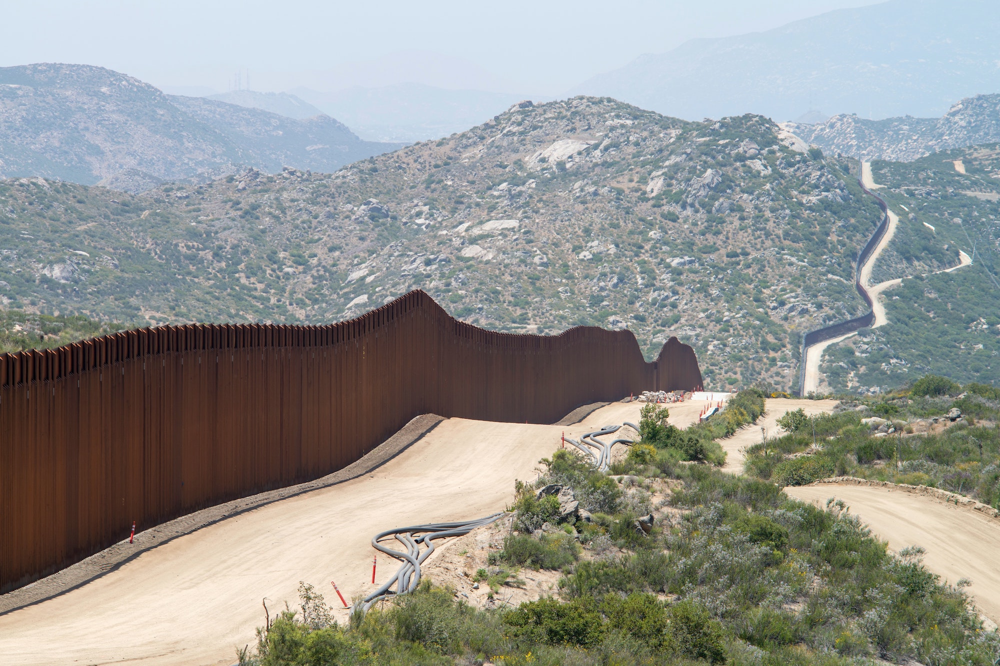 Picture of mountainous scrubland with a reddish brown fence running through the terrain