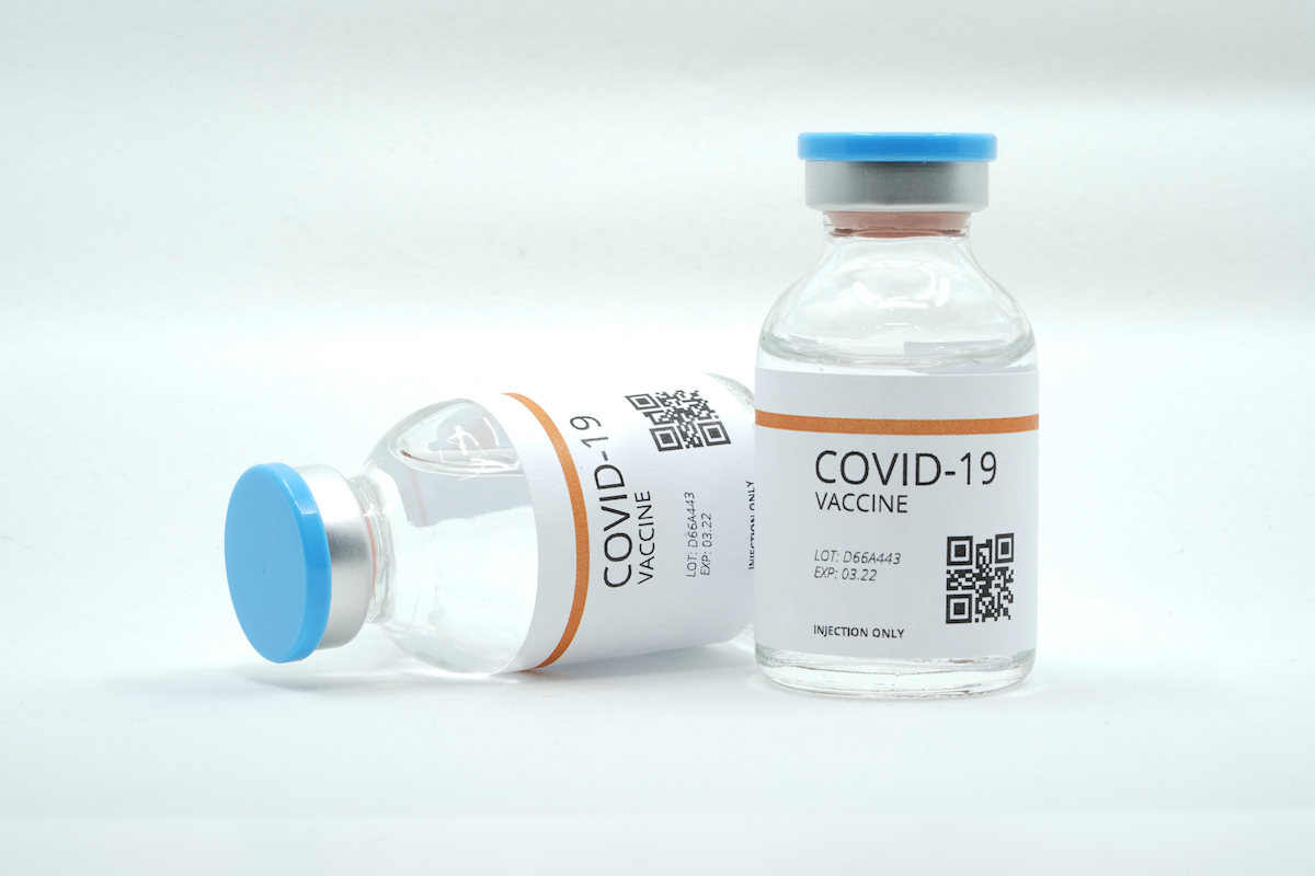 Stock image of two vials of COVID-19 vaccines. One is upright, the other laying on its side. They both say "COVID-19 vaccine, LOT: D66A443, EXP: 03.22, INJECTION ONLY"